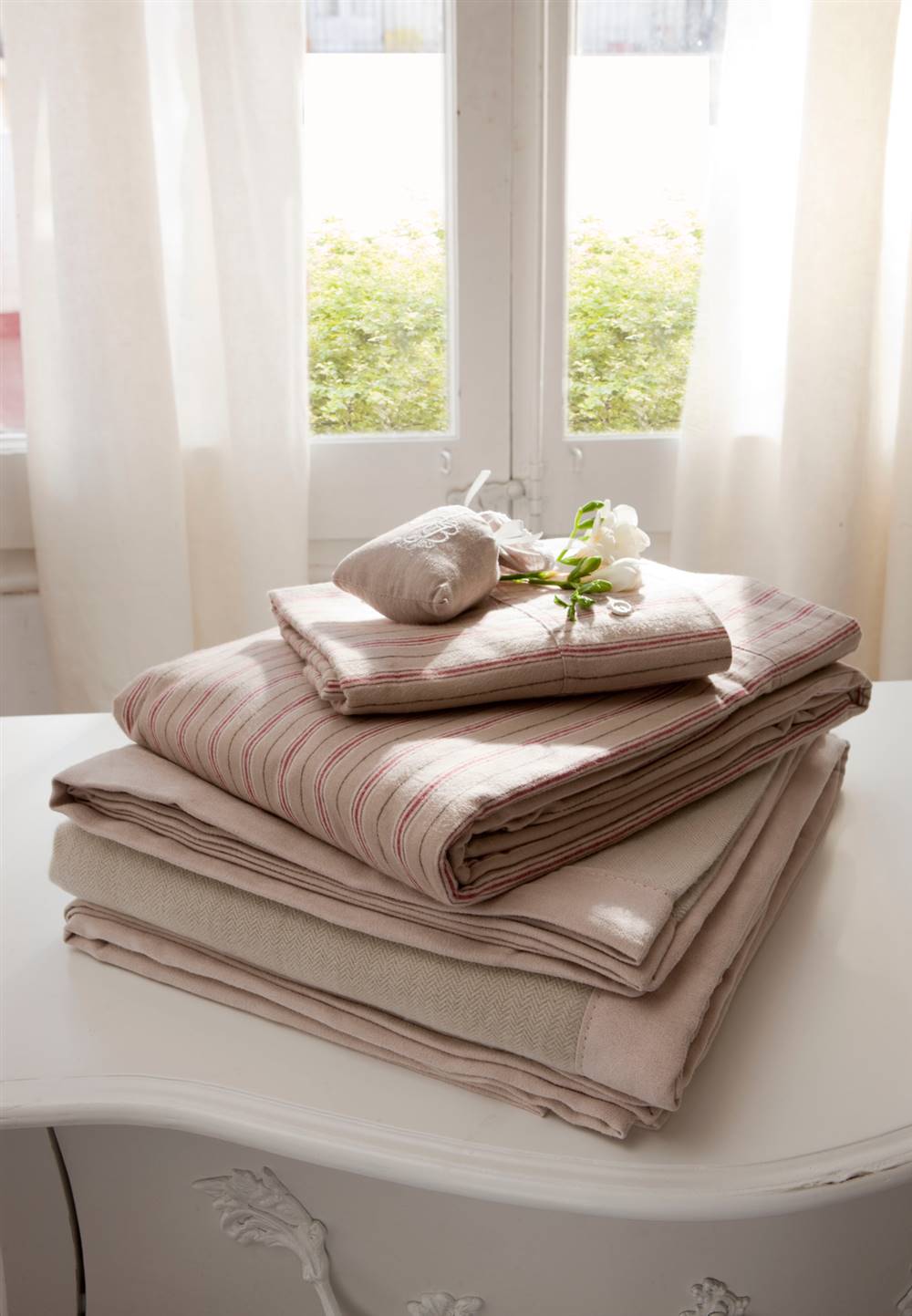 Detalle de sábanas y ropa de cama en tonos rosa y gris sobre consola  312810