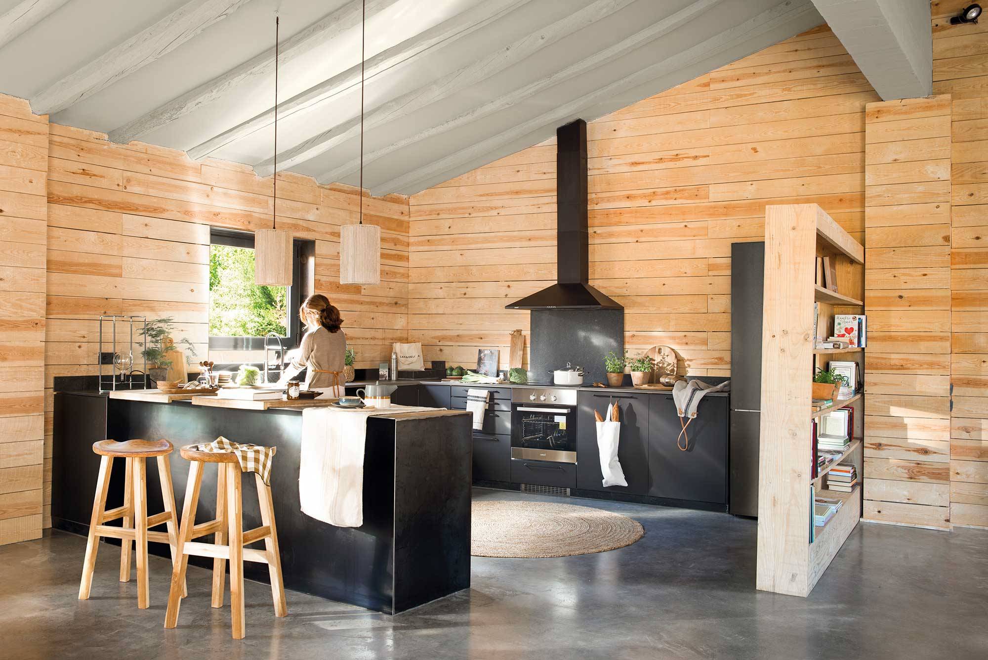 Cocina con paredes de madera y look industrial con muebles en negro.