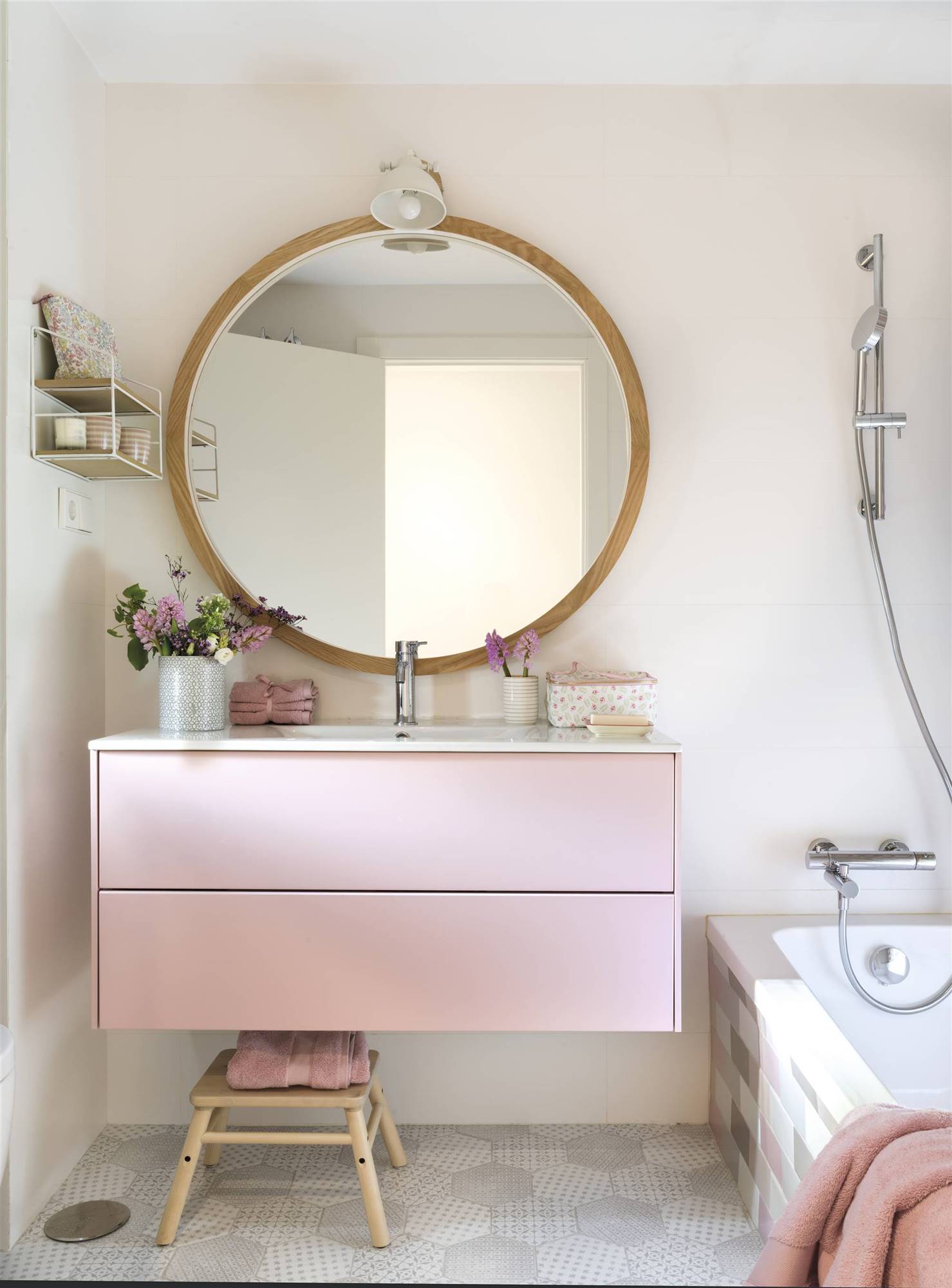 Baño rosa con gran espejo redondo y mueble bajolavabo volado.