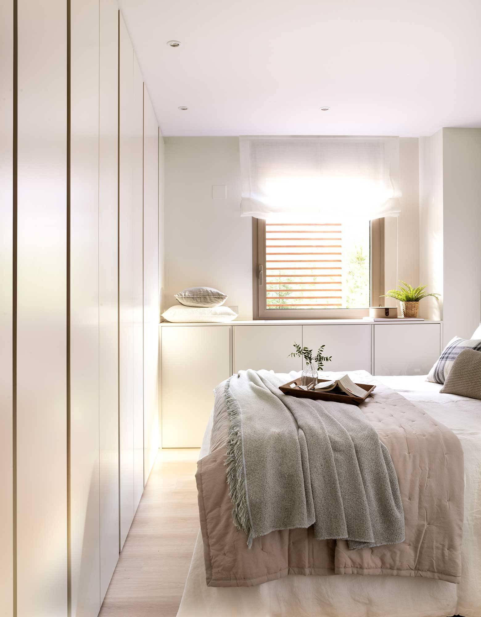 Dormitorio blanco con armario a pie de cama de punta a punta.