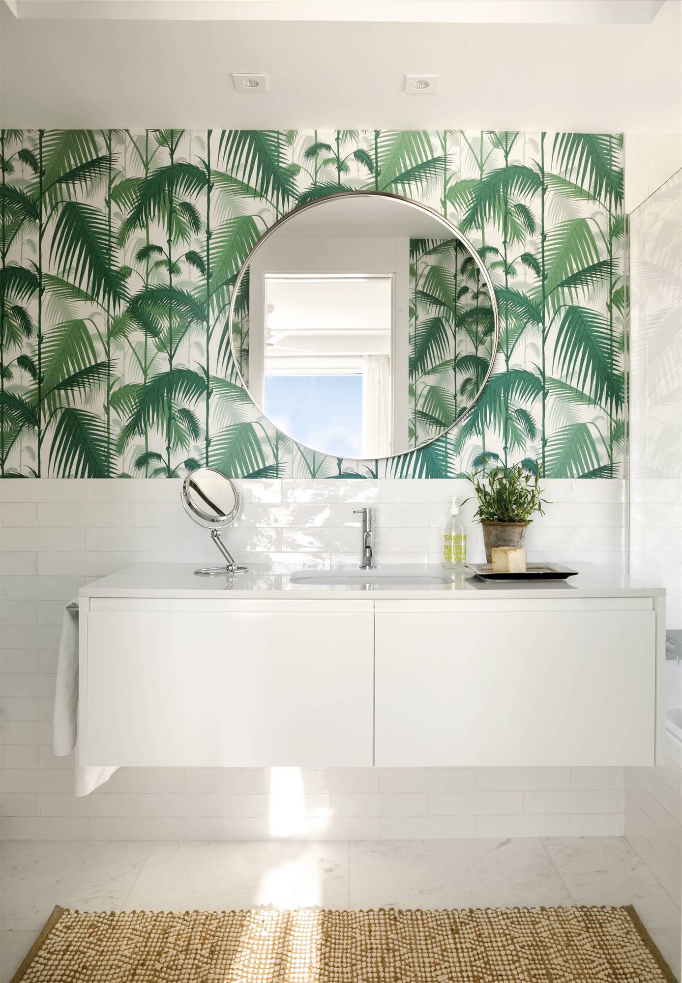 Baño blanco con mueble volado y pared con papel pintado de palmeras.