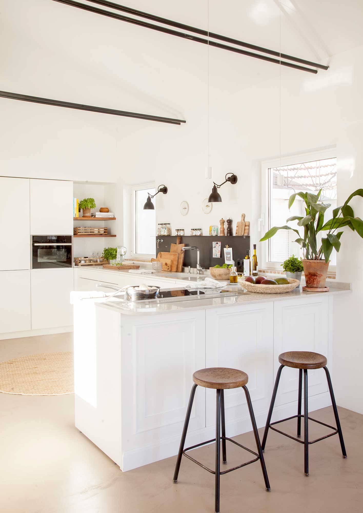 Cocina blanca de diseño con barra con taburetes y muebles lisos.