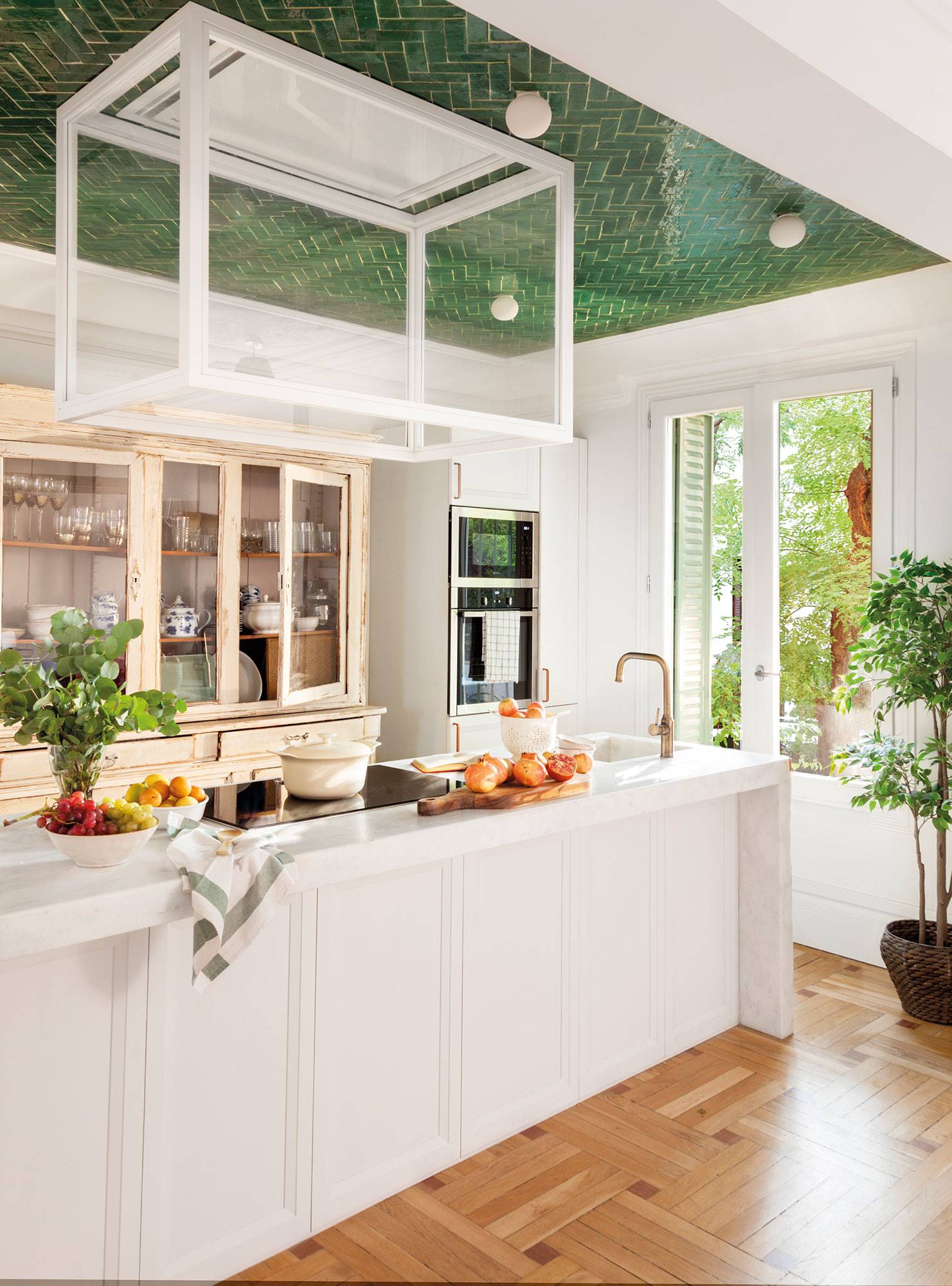 Cocina de diseño con barra blanca, campana extractora moderna de cristal, azulejos verdes en el techo y alacena antigua recuperada.