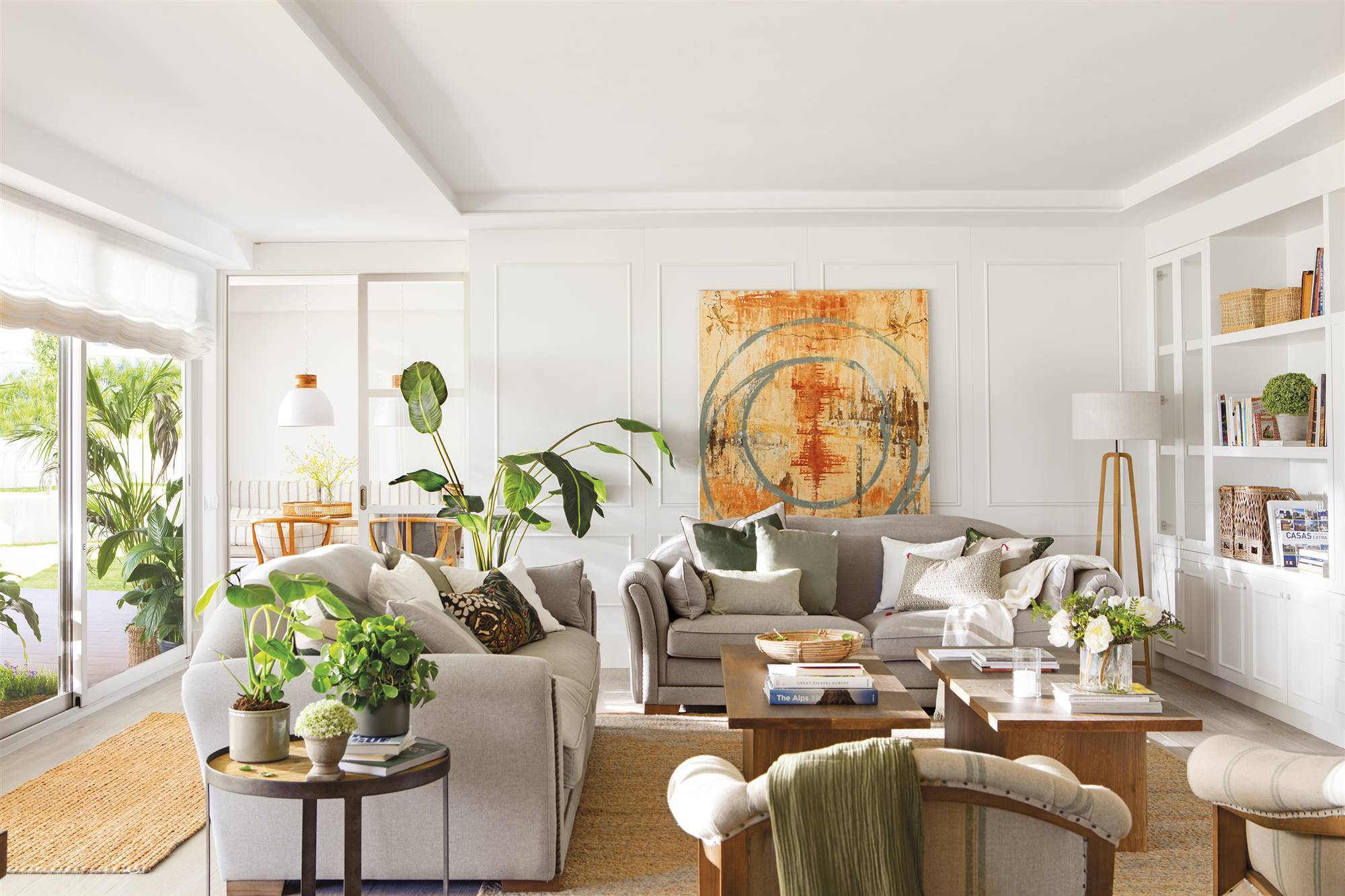 Salón con molduras, sofás en gris, estantería blanca, cuadro y plantas.