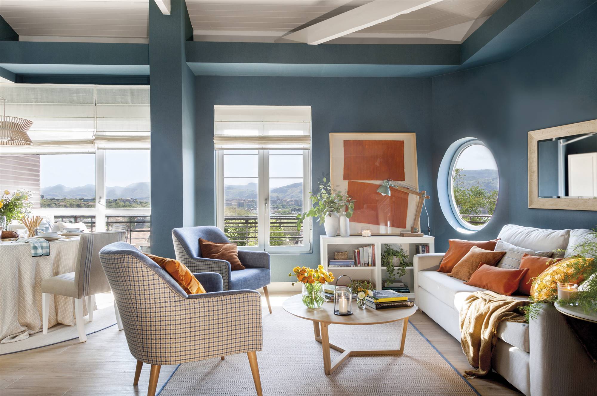 Salón empapelado de azul con sofá neutro y comedor al fondo.