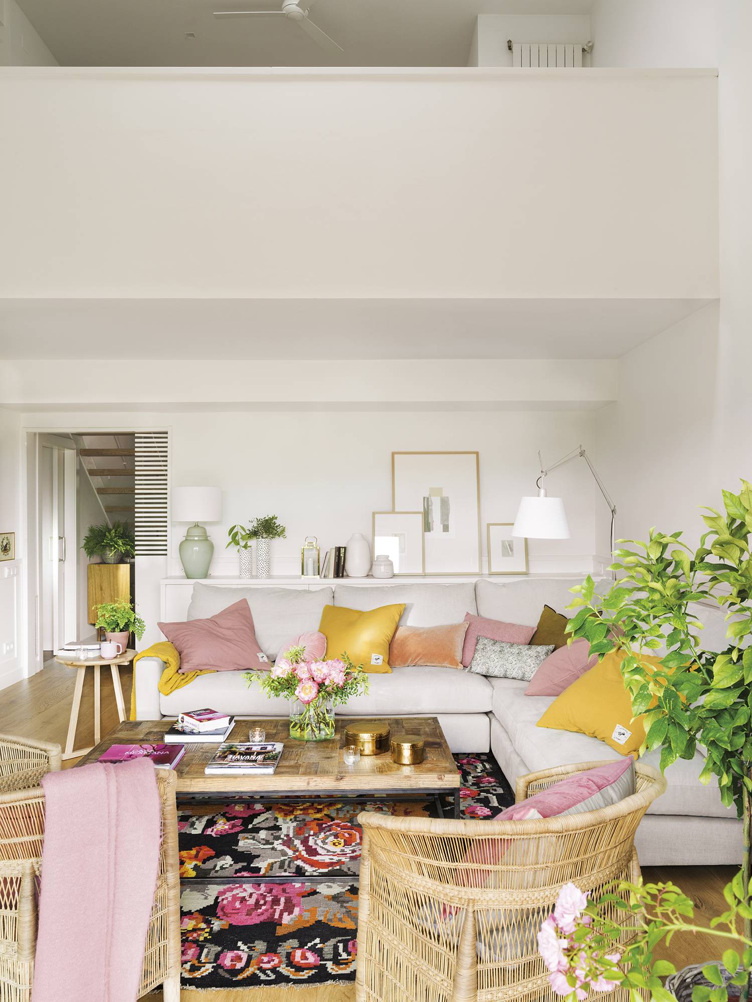 Salón con sofá en L, butacas de fibras, alfombra con motivos florales, y cojines en tonos rosas y mostazas FER3407