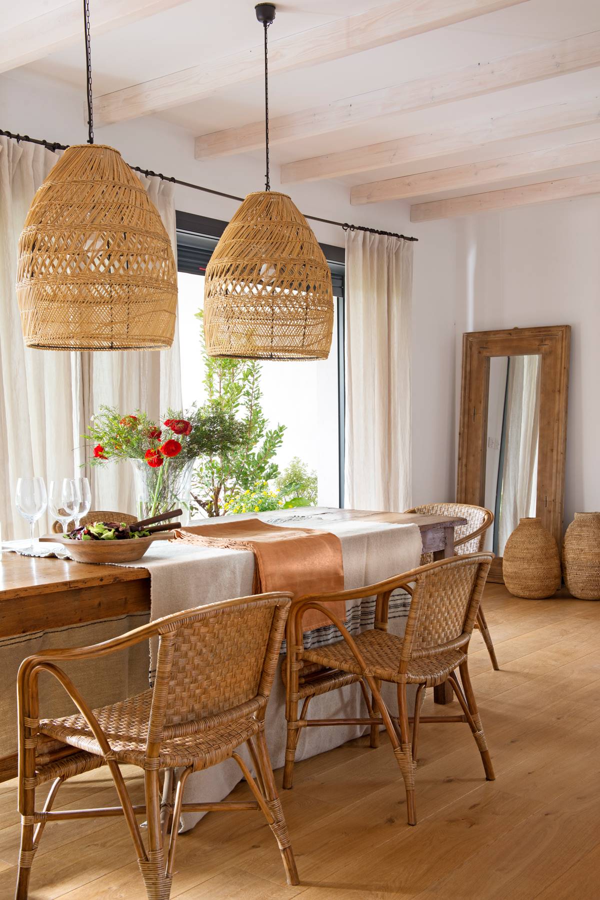 Comedor con mesa de madera, y lámparas, sillas, espejo y cestos de fibra natural. 