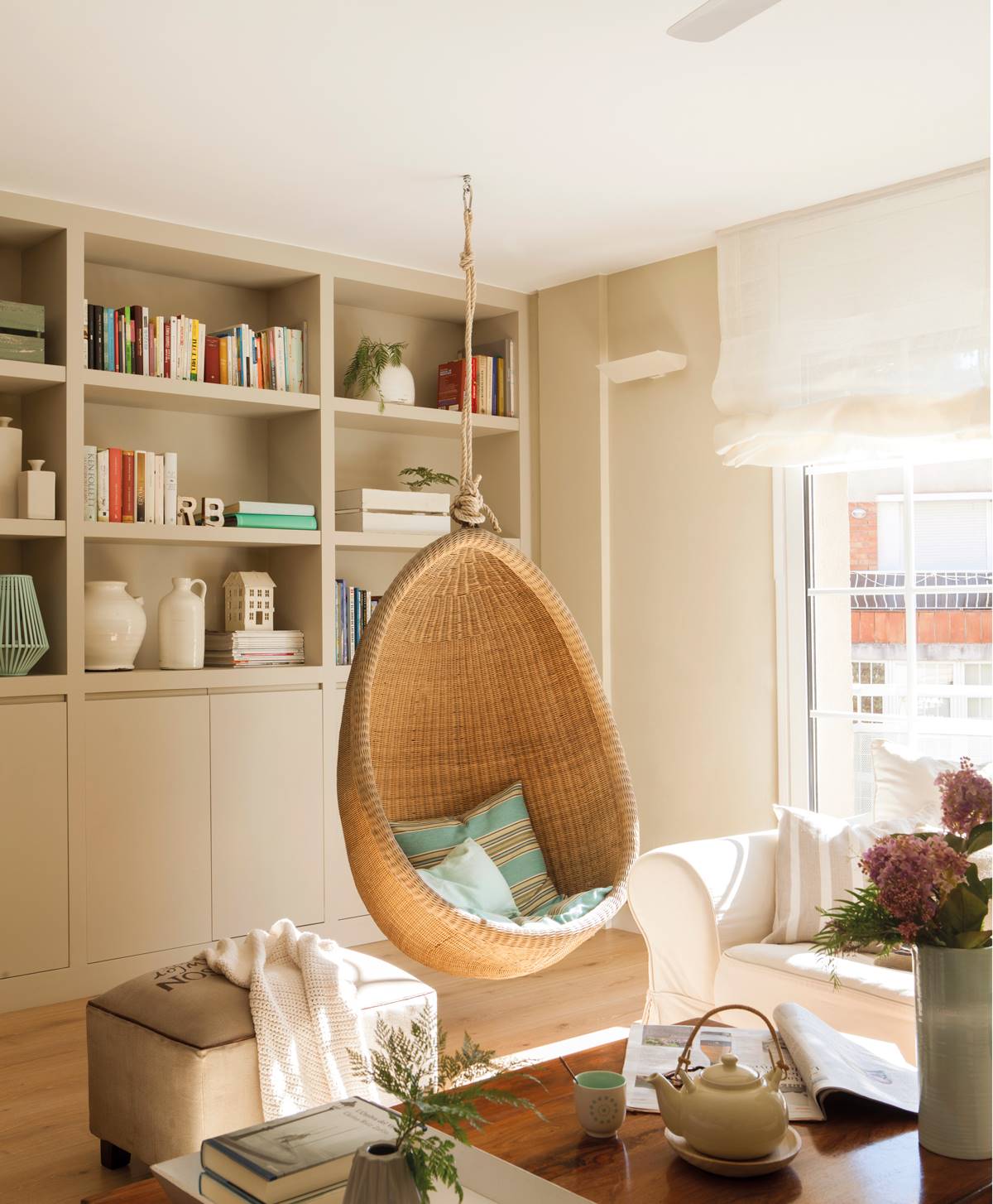 Salón con sillón colgante como columpio de fibras naturales, estantería y sofá blanco. 