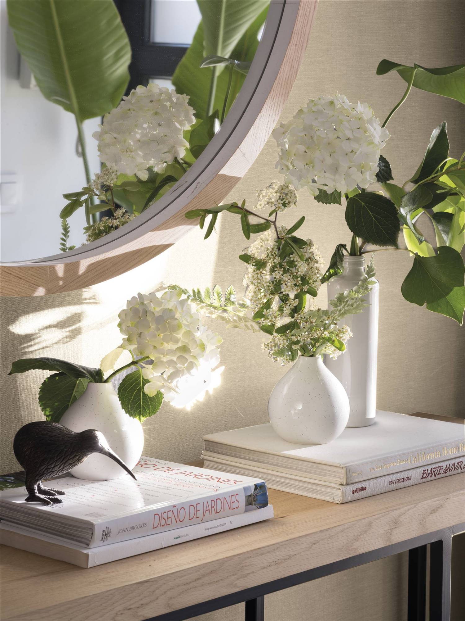 Detalles de recibidor claro con espejo redondo, plantas y libros.