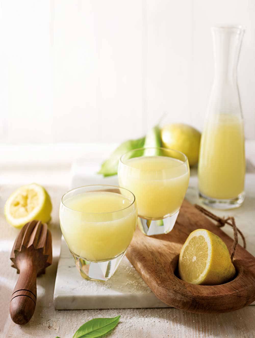 Vasos y jarra con zumo de limón sobre tabla de madera y mármol y limones naturales partidos