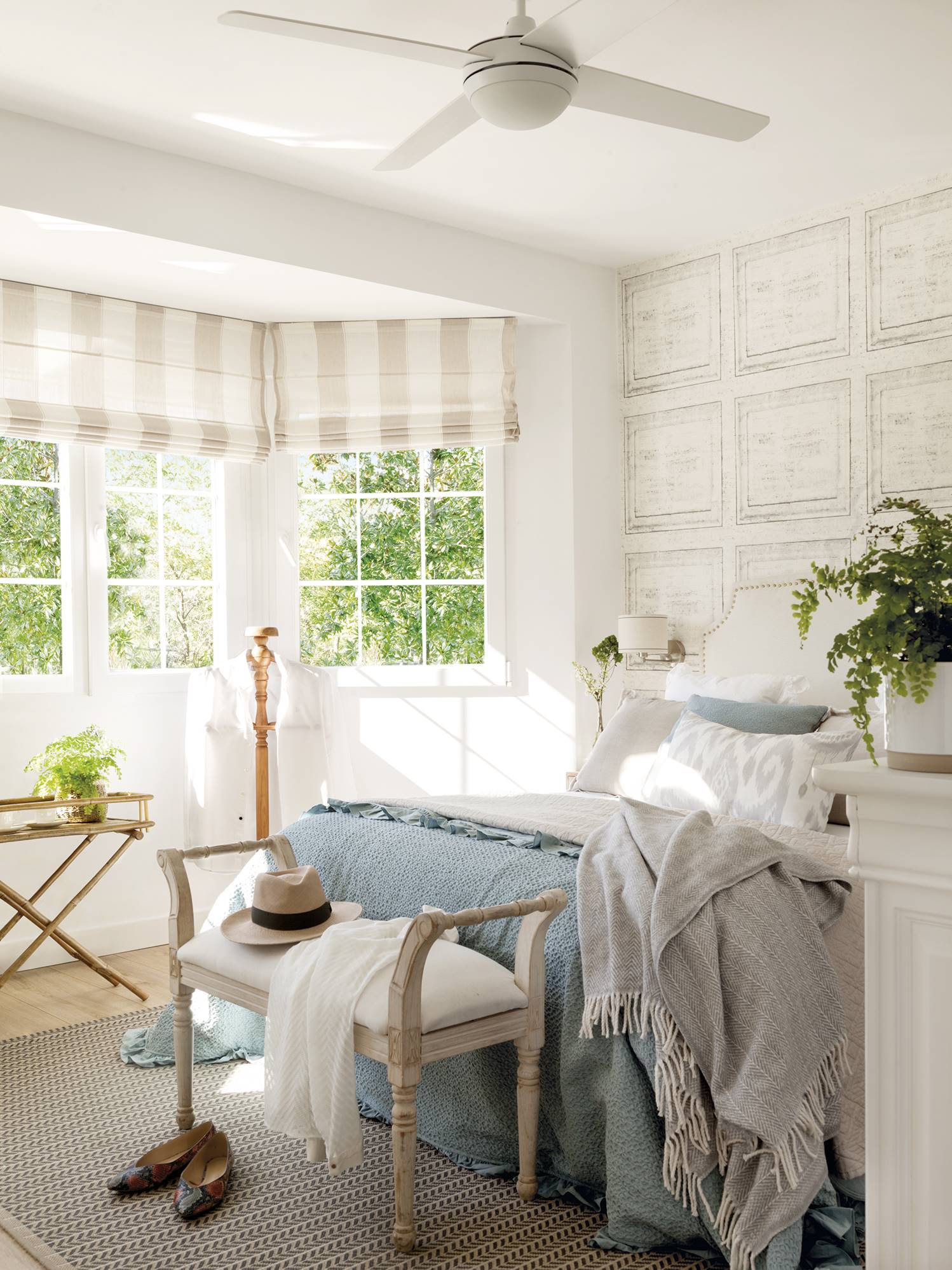 Dormitorio principal con papel pintado, ventilador y banco a los pies de la cama.