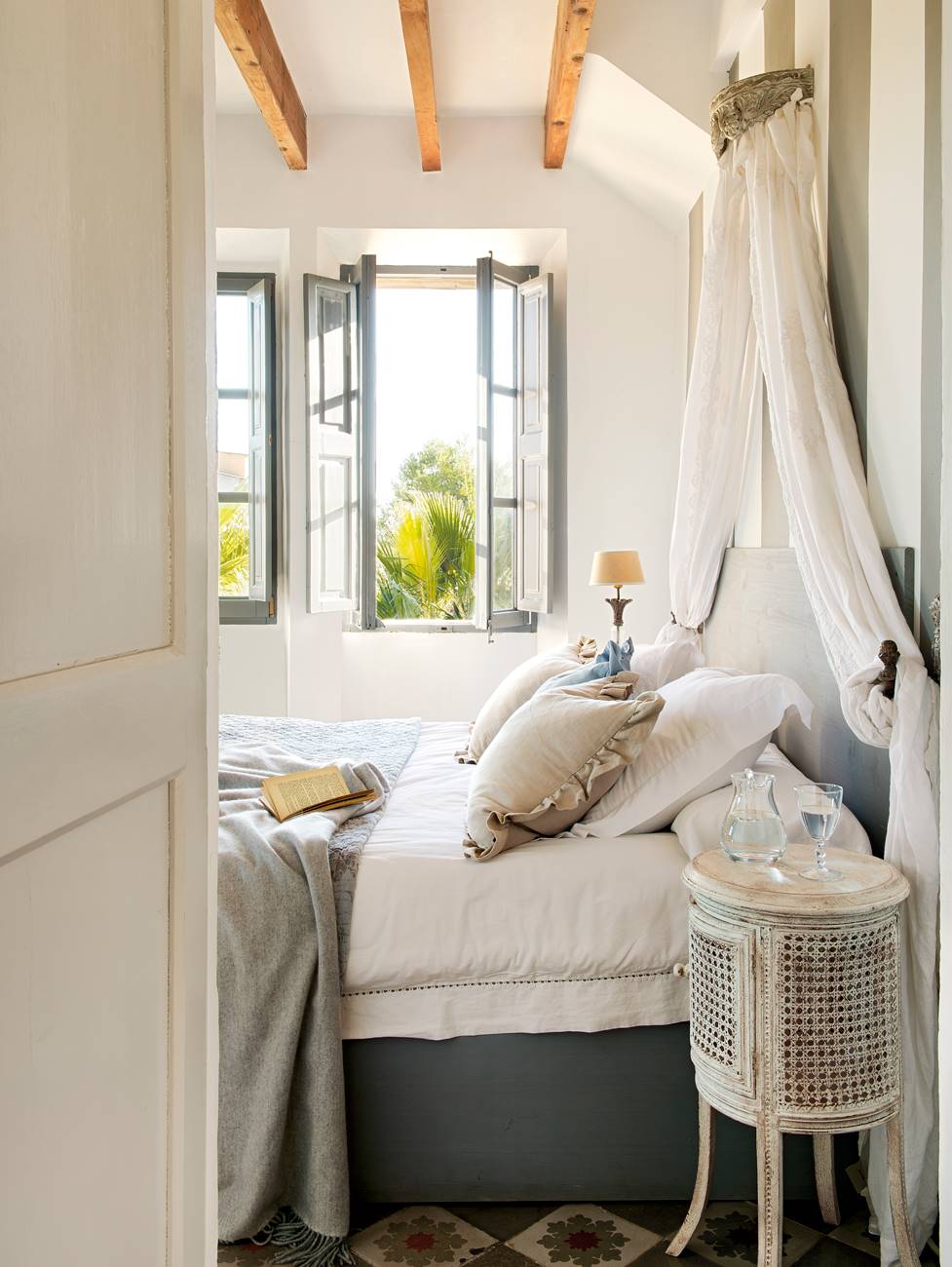 Dormitorio con mesilla de noche de mimbre, vigas de madera, ventana con porticones de color azul y mosquitera (00378440-Mesillas)