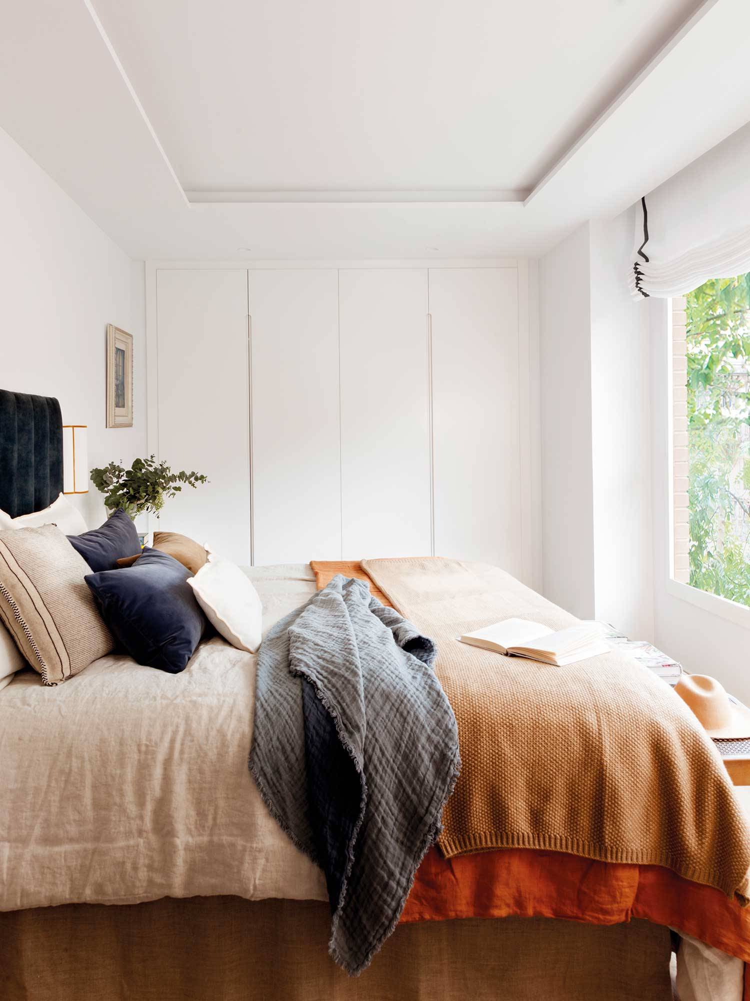 Dormitorio moderno con cabecero de terciopelo azul y ropa de cama color arena y caldero. 