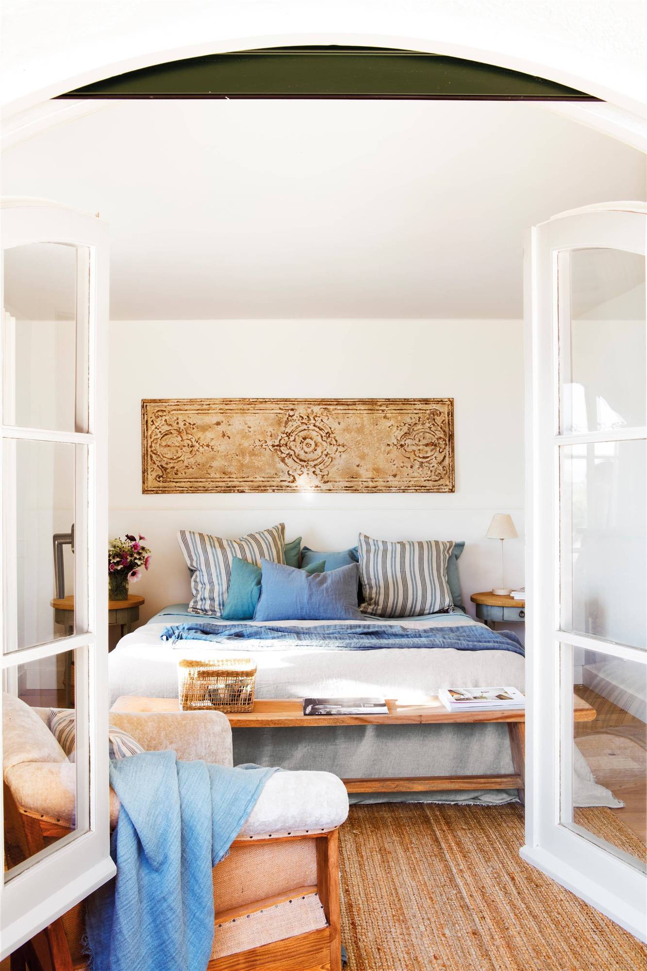 Dormitorio de verano con cojines de rayas marineros y cuadro de madera en pared. 