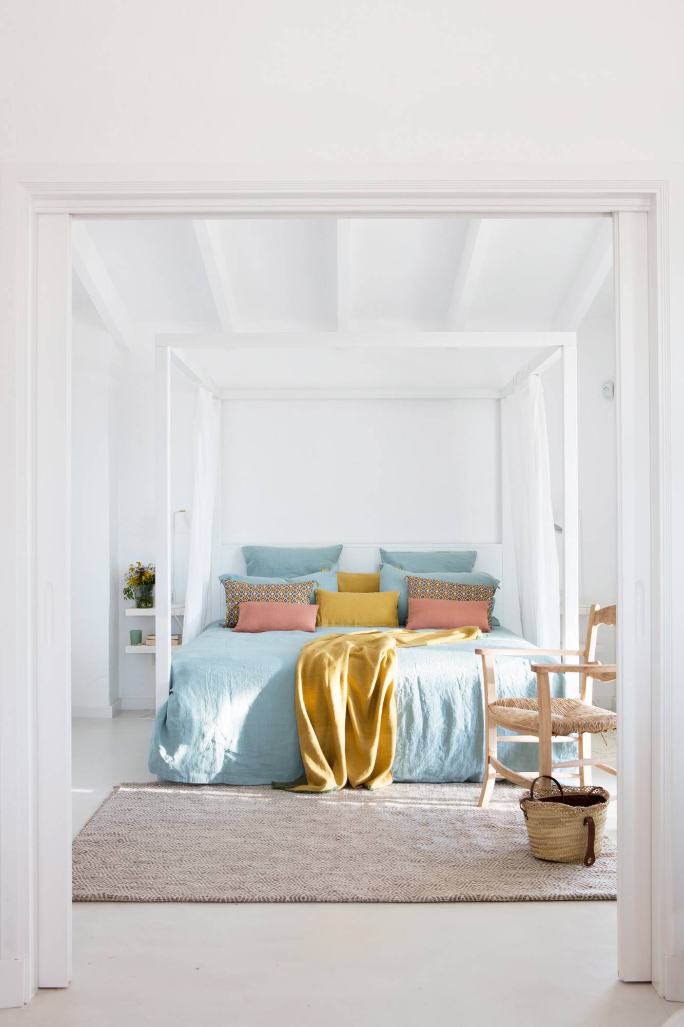 Dormitorio moderno con cama con dosel blanco y ropa de cama en tonos azules.