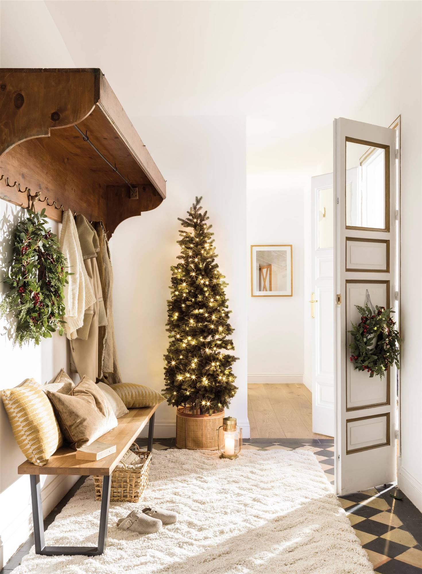 Recibidor con perchero de madera, banco zapatero, alfombra de pelo blanco y corona navideña en puerta de entrada 00515385