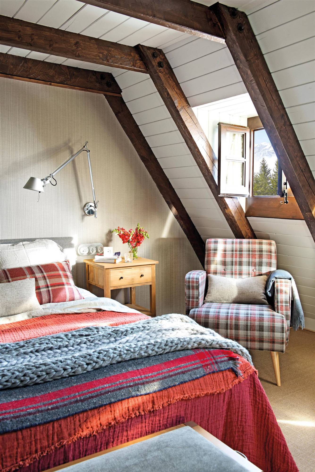 Dormitorio con butaca con tapicería de cuadros y ropa de cama en tonos rojos y azules