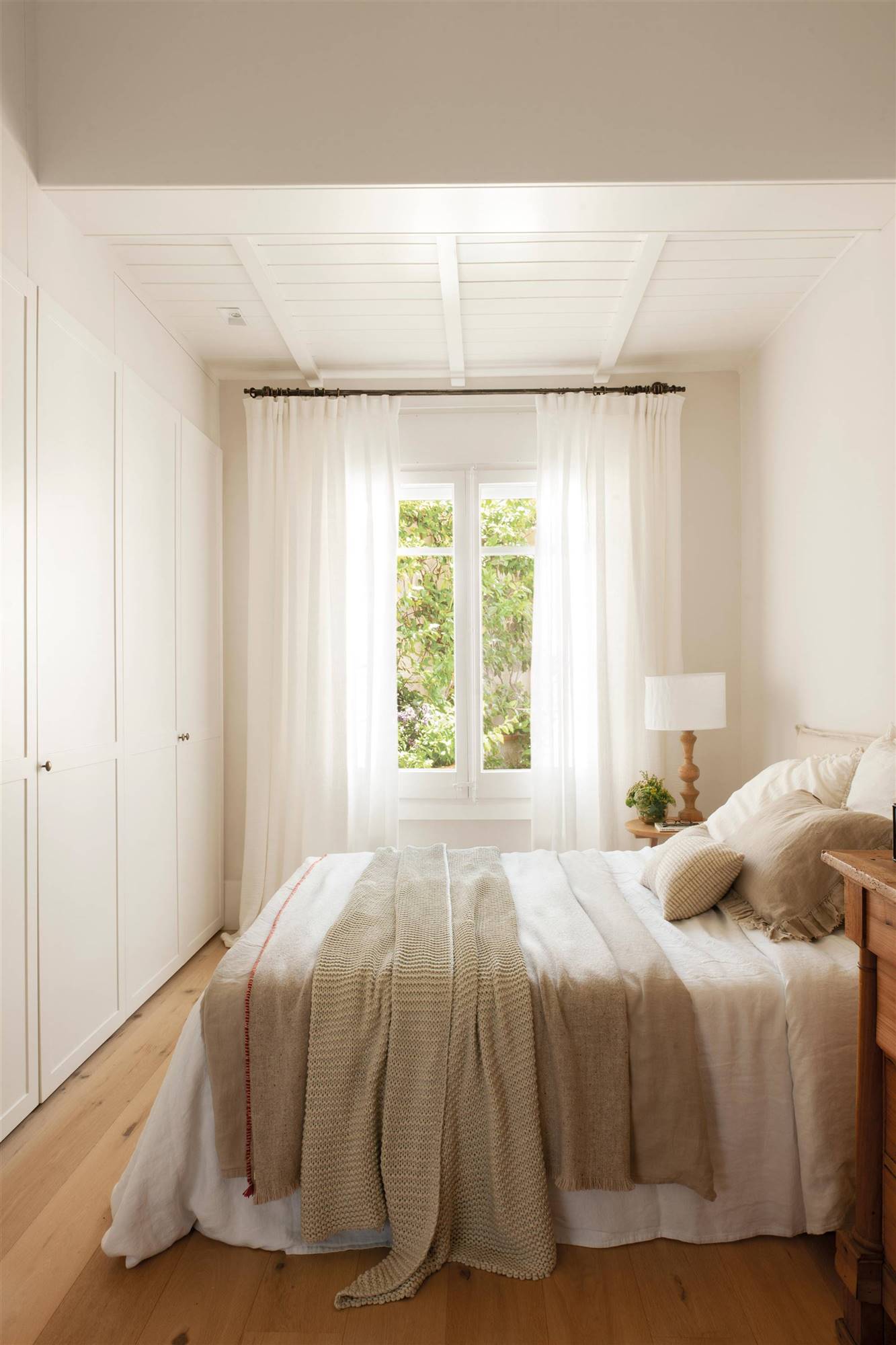 Dormitorio en blanco con el techo bajado decorado con cuadrícula y aramario empotrado frente a la cama..