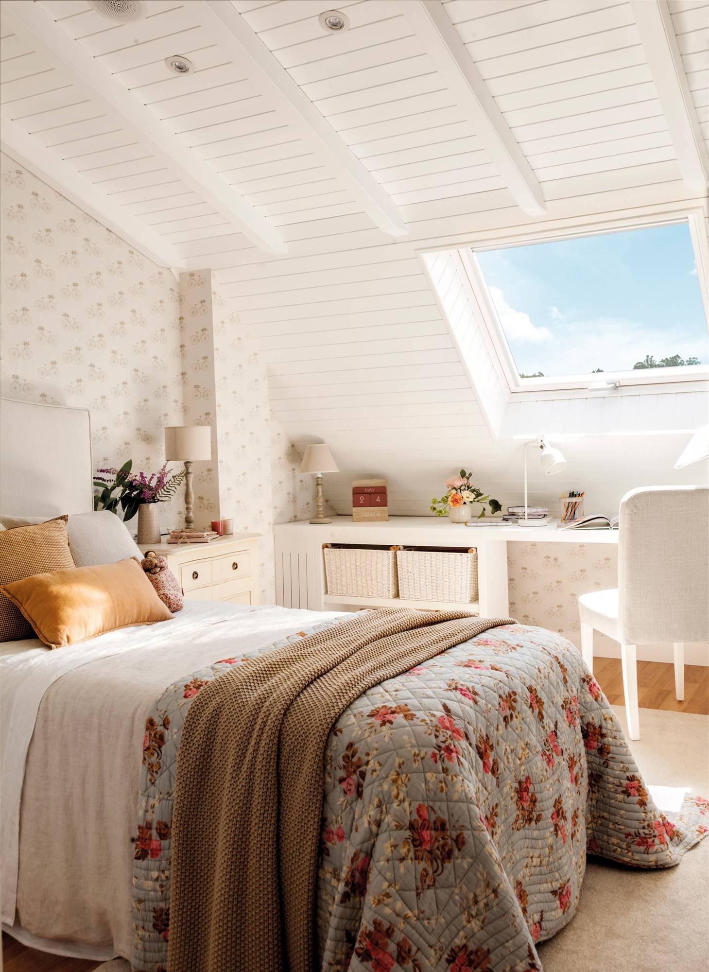 Dormitorio blanco con pared de cabecero revestido de papel pintado, escritorio bajo la ventana y boutí de flores.