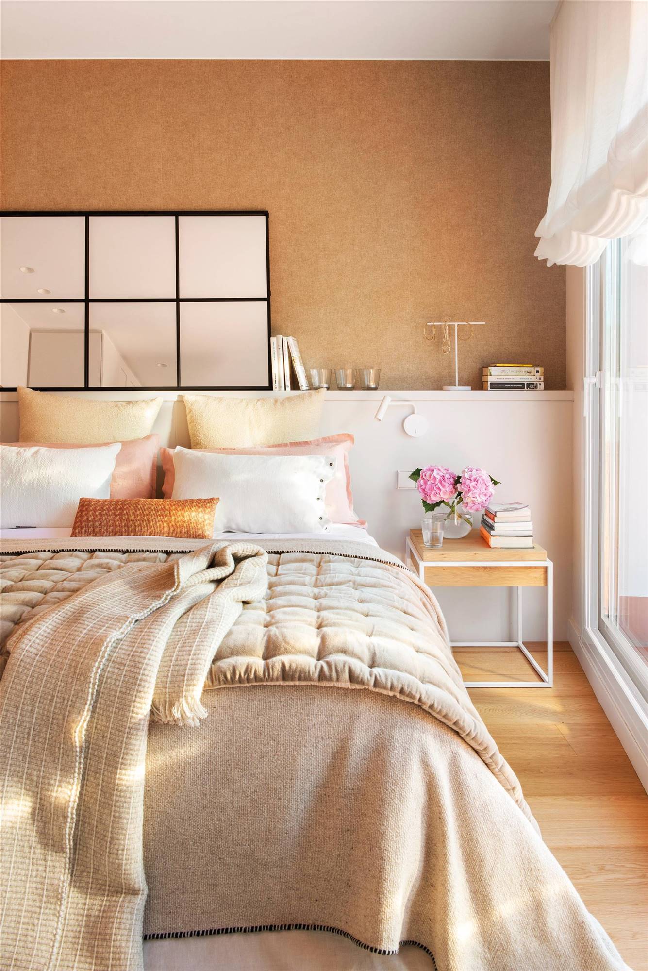 Dormitorio con cabacero de obra blanco, pared revestida de papel pintado en color arena y espejo de cuadrícula..