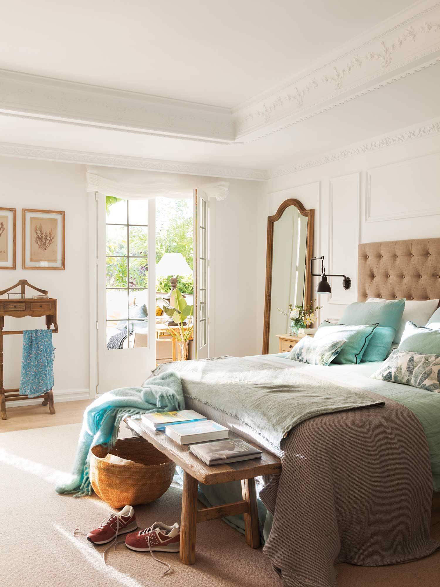 Dormitorio clásico con cabecero de capitoné beige y ropa de cama blanca y azul. 