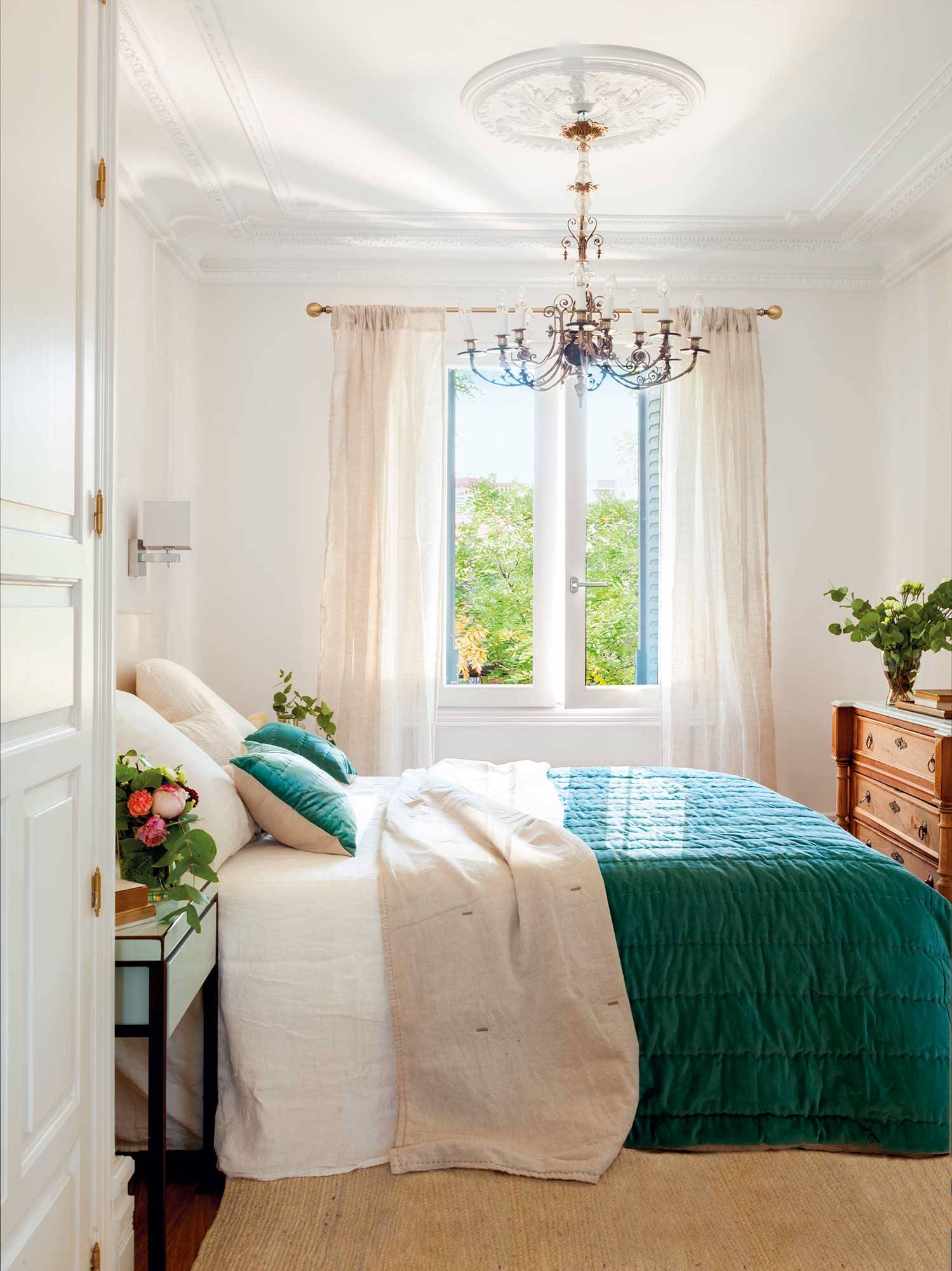 Dormitorio con ropa de cama blanca y azul, lámpara de araña y cómoda de madera. 