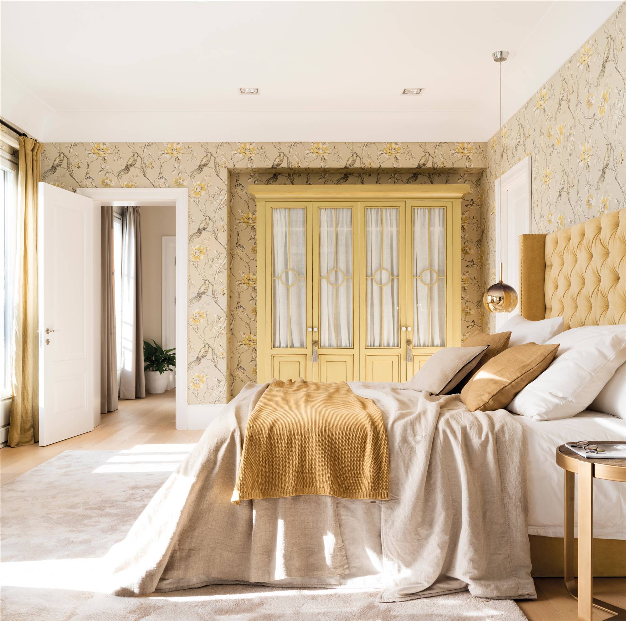 Dormitorio clásico con cabecero de capitoné y armario en color mostaza y papel pintado floral. 