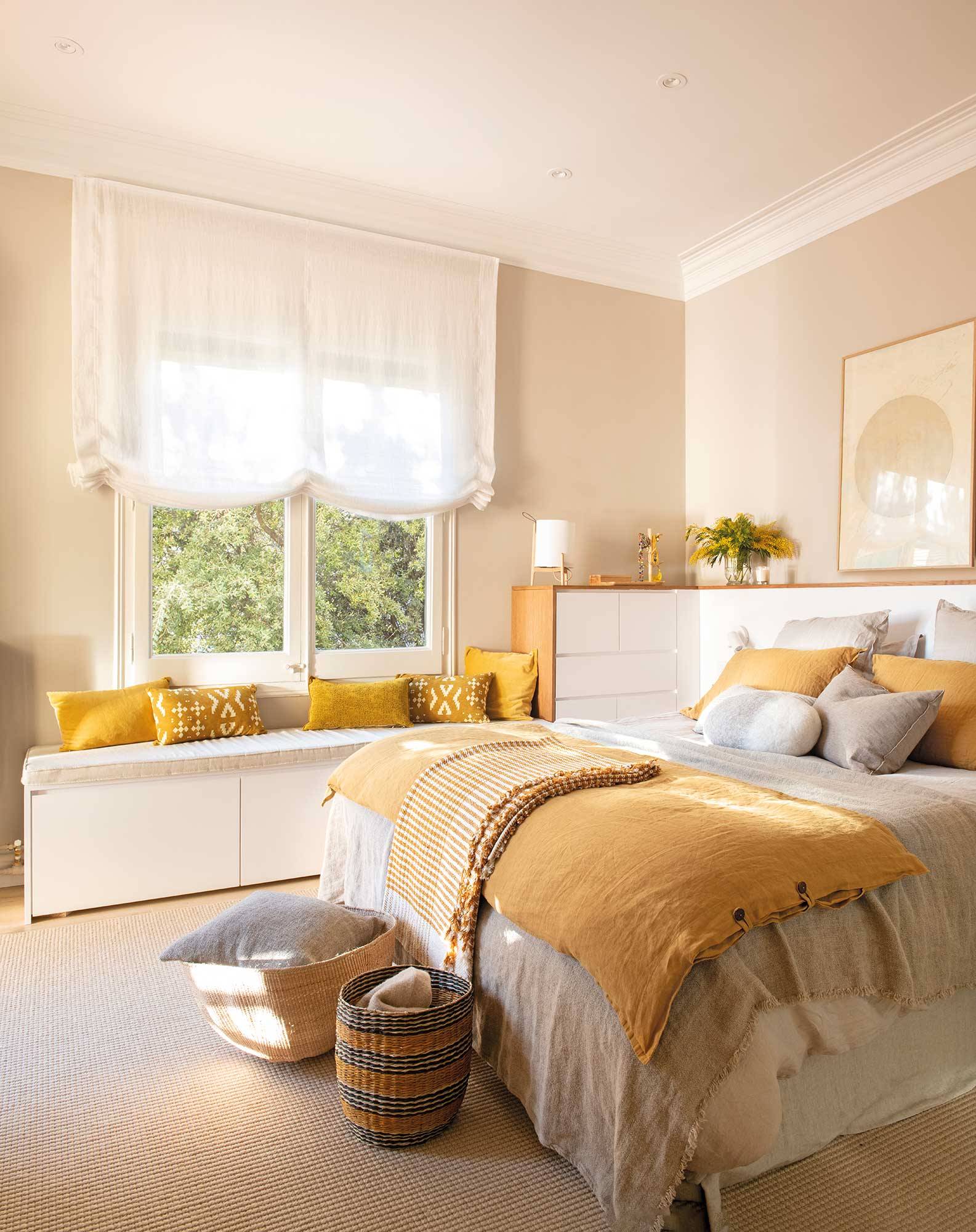 Dormitorio con banco a pie de cama y textiles blancos y amarillos. 