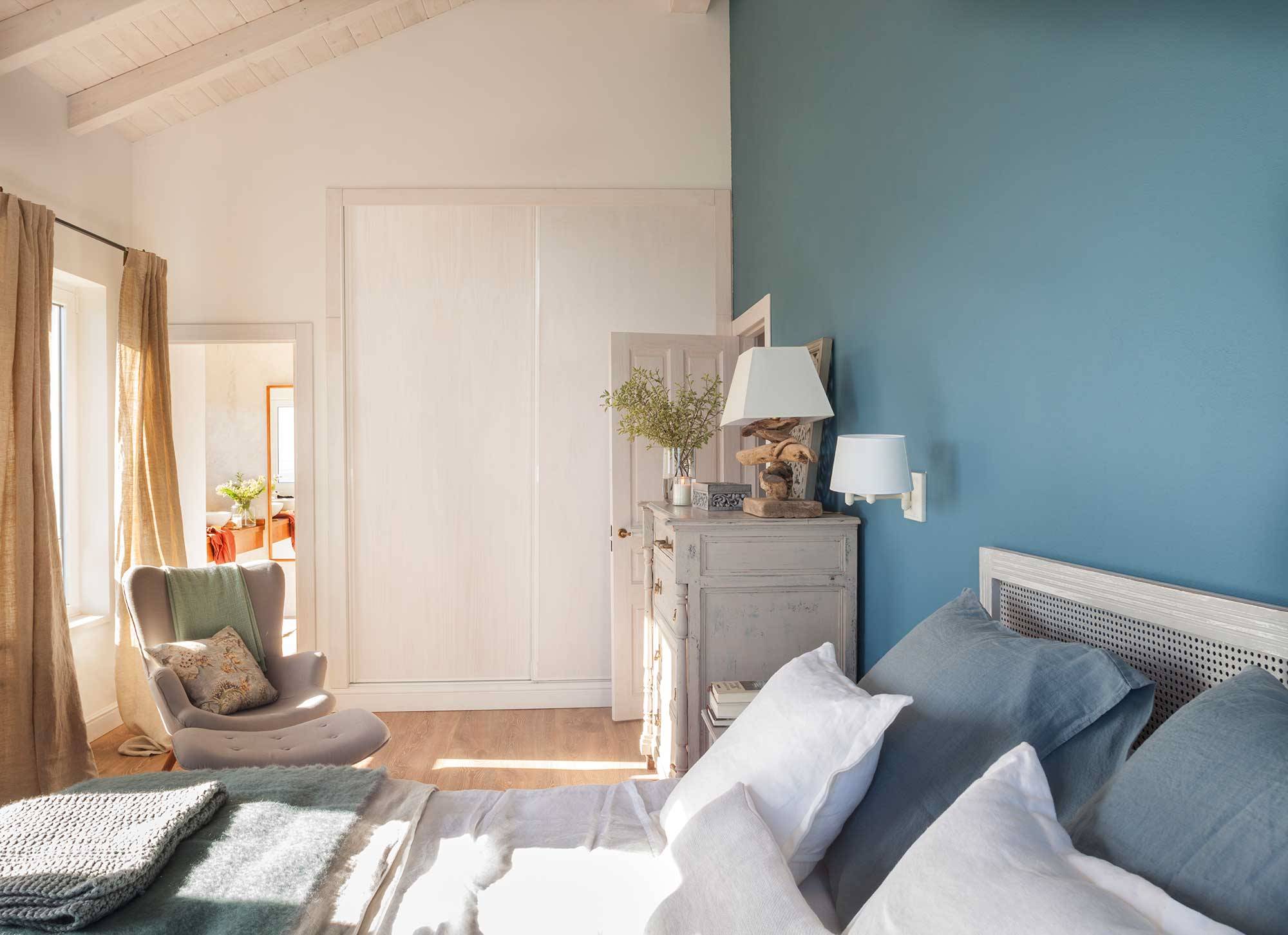 Dormitorio azul grisáceo con butaca y muebles antiguos.