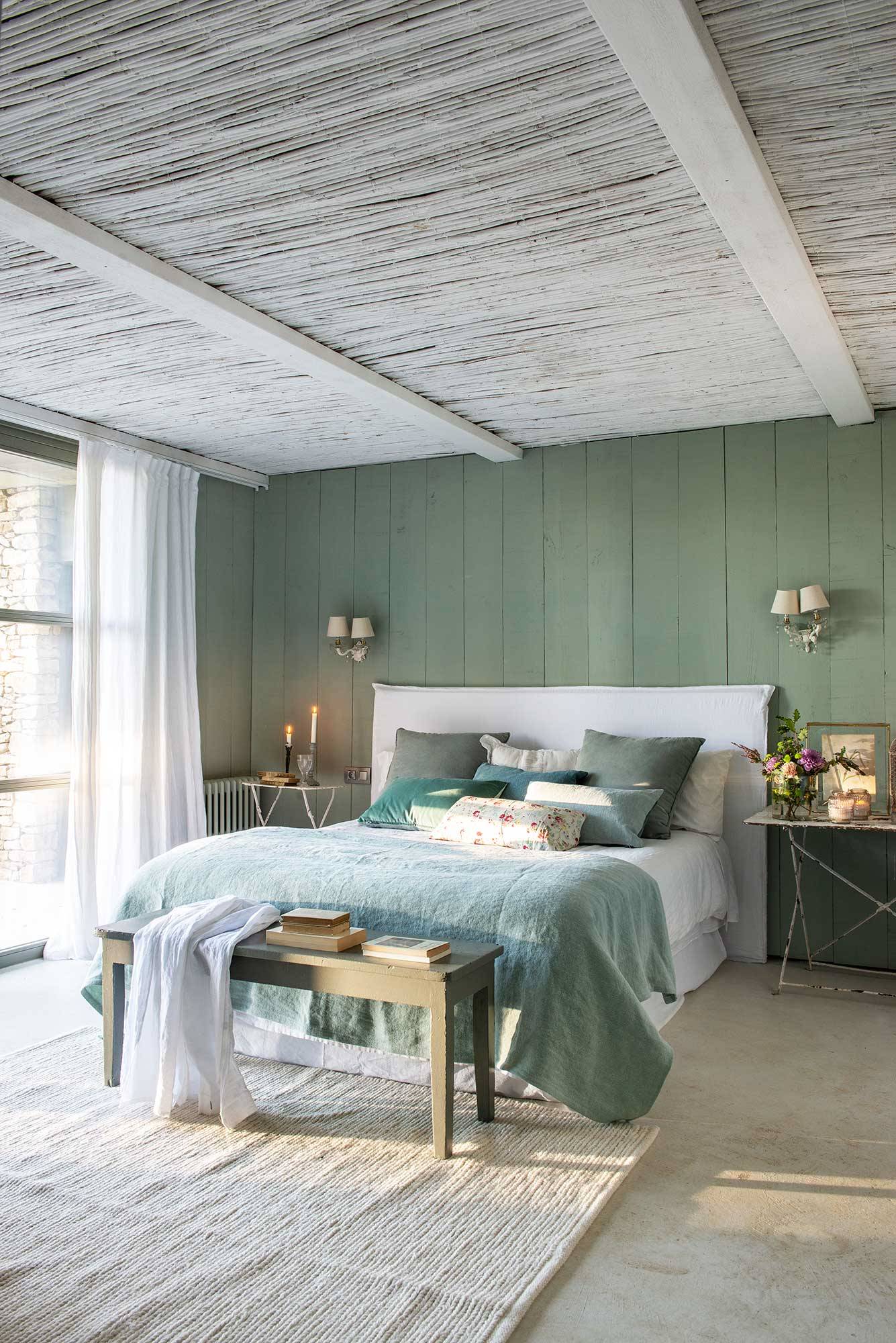 Dormitorio principal con cabecero tapizado y revestimiento de madera pintada.