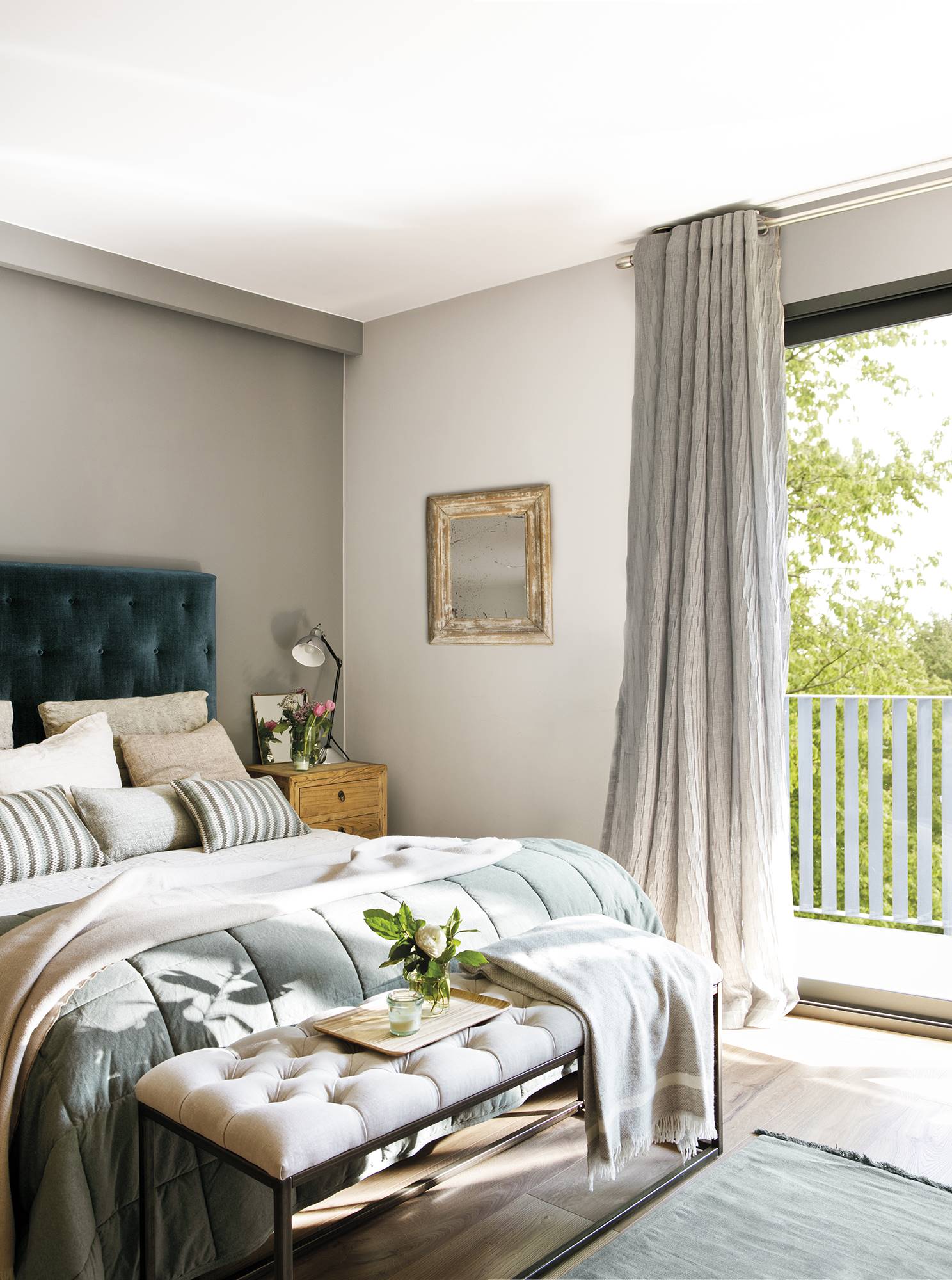 Dormitorio gris con cabecero tapizado de capitoné, banco y cortinas.