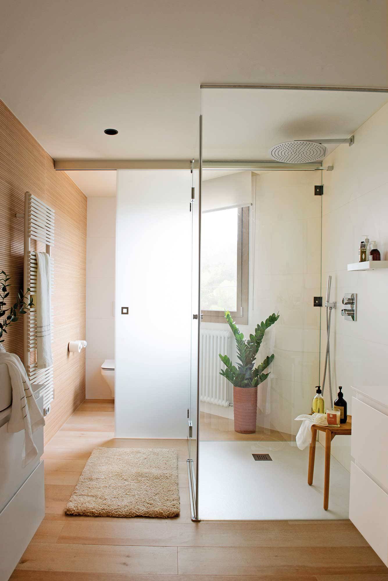 Baño blanco moderno con cabina de sanitarios transparente.