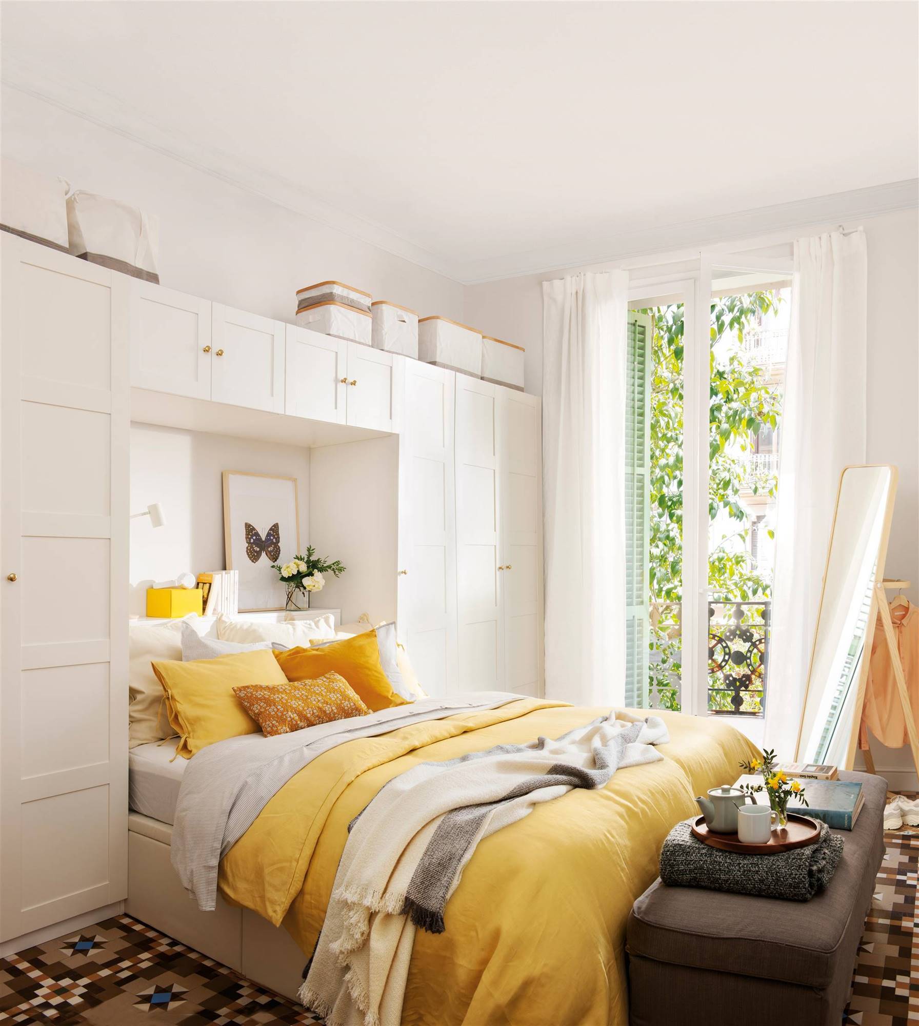 Dormitorio con ropa de cama amarilla y armario de IKEA blanco alrededor de la cama.