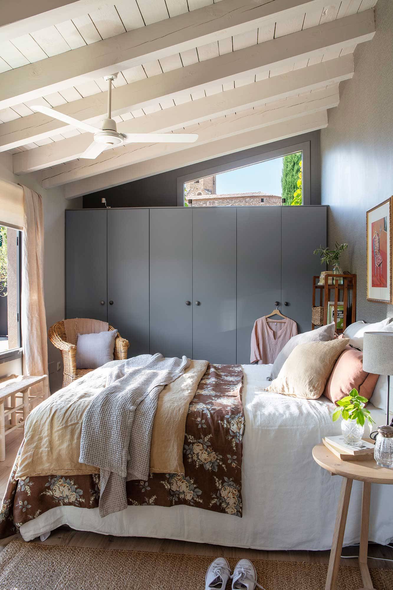 Dormitorio principal con techo abuhardillado, armarios a medida pintados en gris oscuro y mesita de noche de La Maison. 