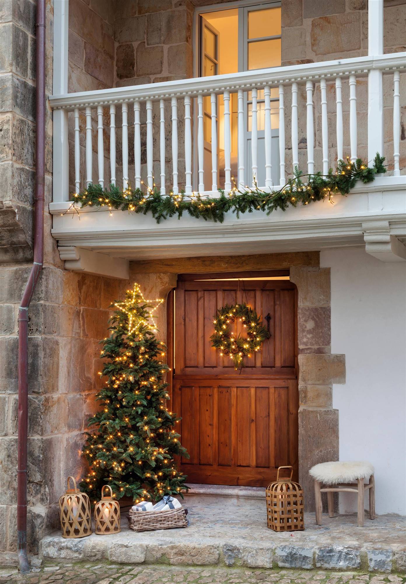 Puerta de entrada de madera con árbol de Navidad iluminado y corona navideña.