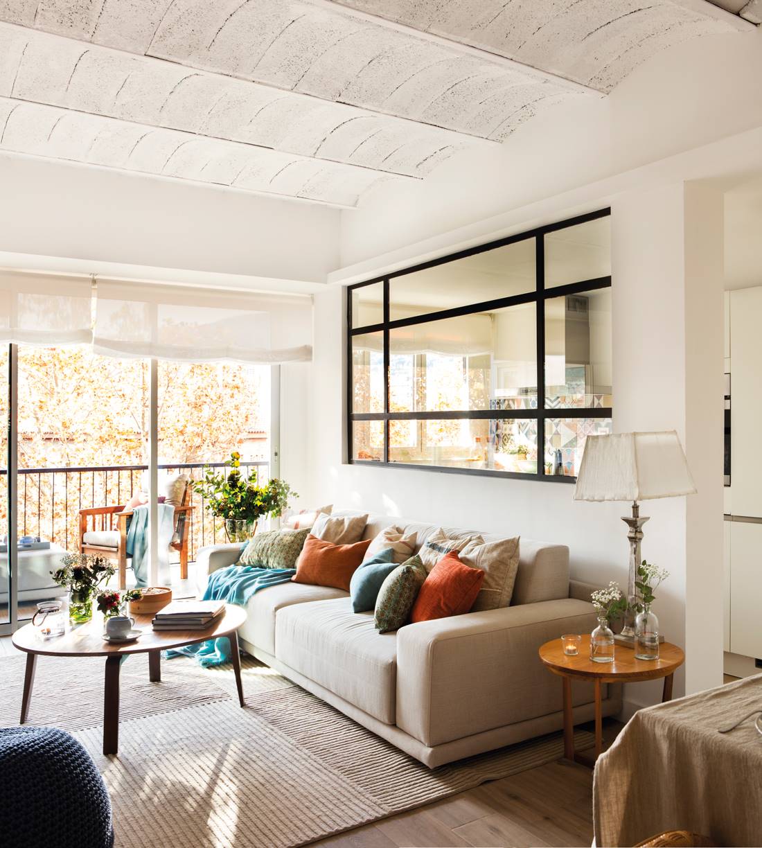salón pequeño con sofá gris y ventana fija que comunica con cocina 00449671