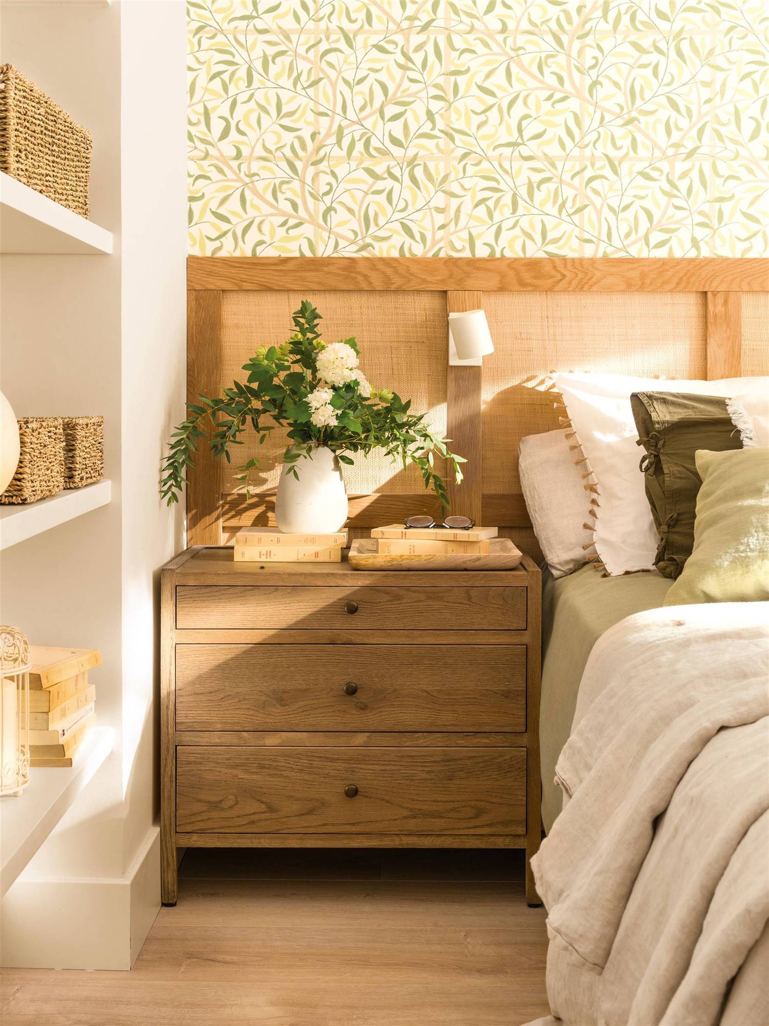 Dormitorio con papel pintado, mesa de noche de madera y cabecero personalizado de rafia. 