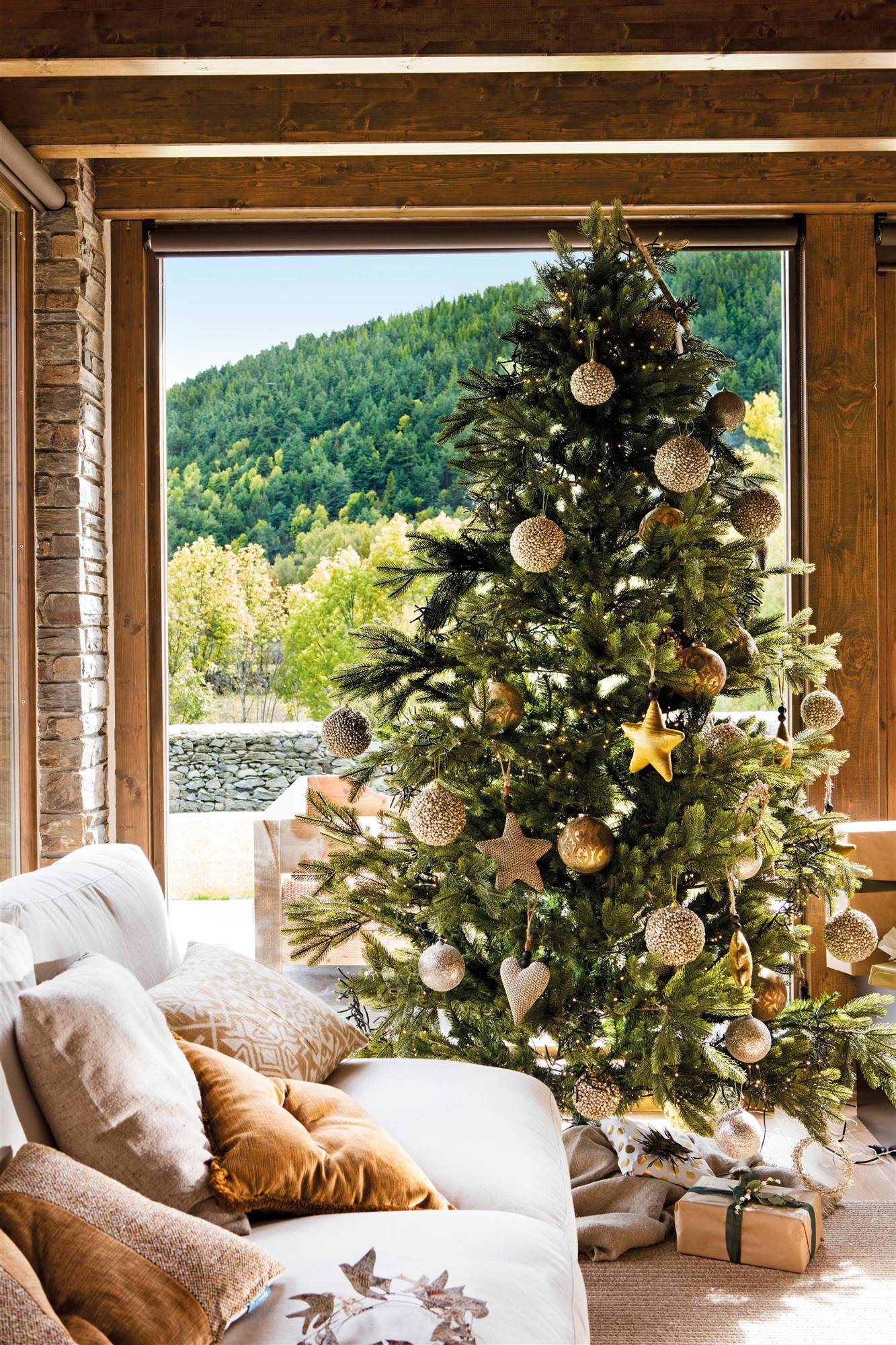 Salón rústico con árbol de Navidad decorado con adornos dorados y plateados. 