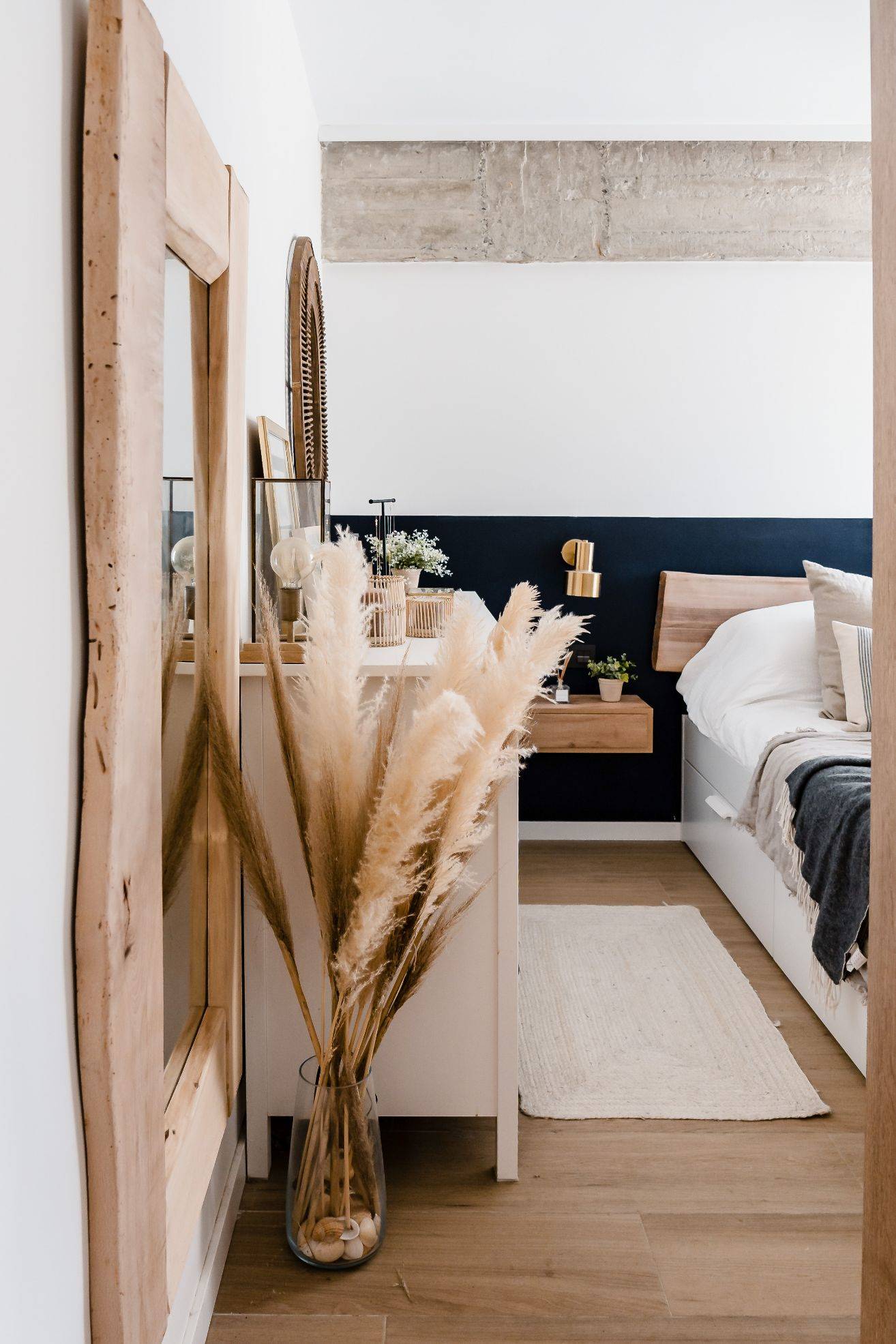 Dormitorio después de la reforma muy natural con flores secas y espejo de madera clara. 