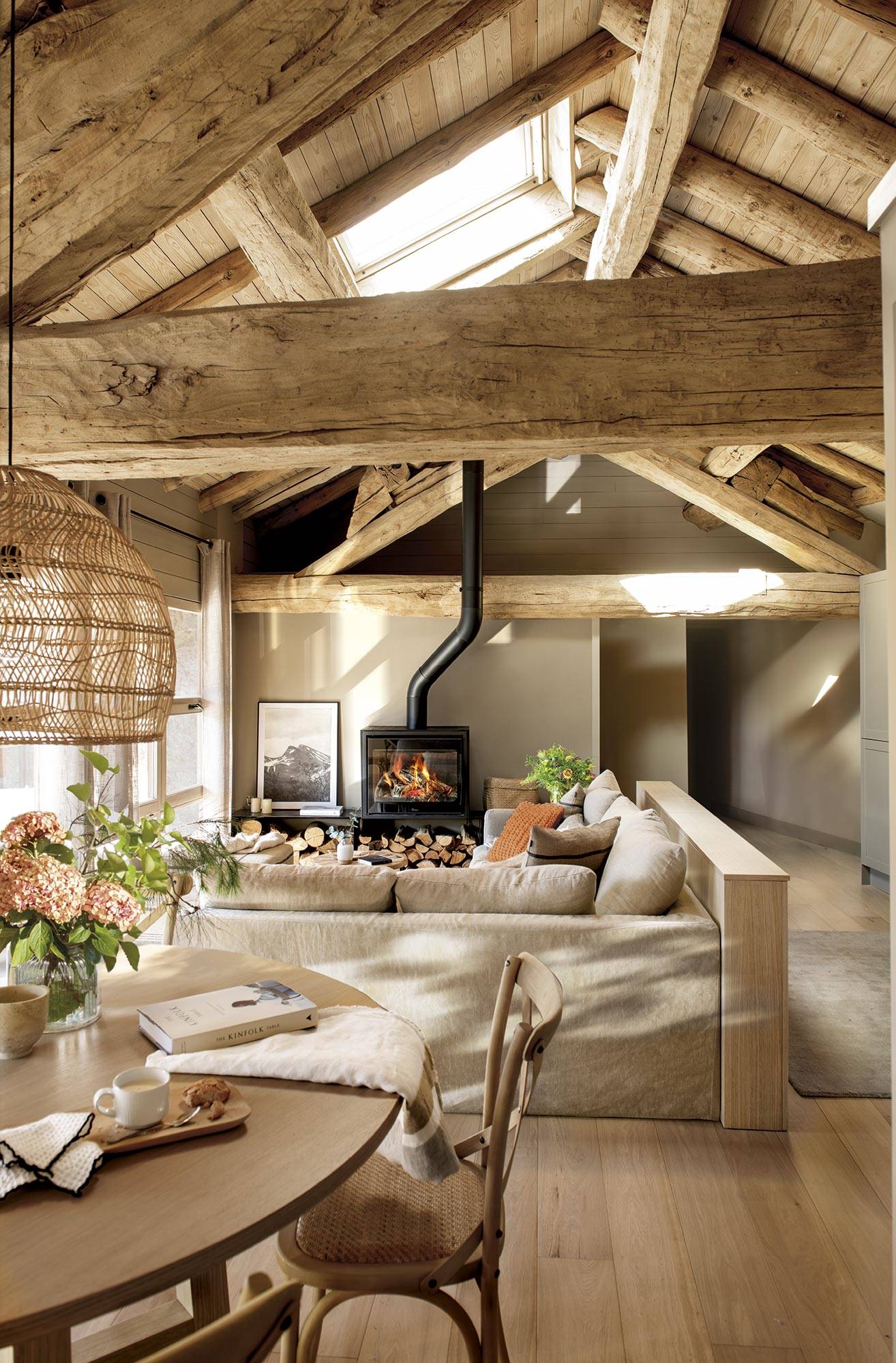 Salón comedor con sofá beige, techo de vigas de madera y chimenea. 