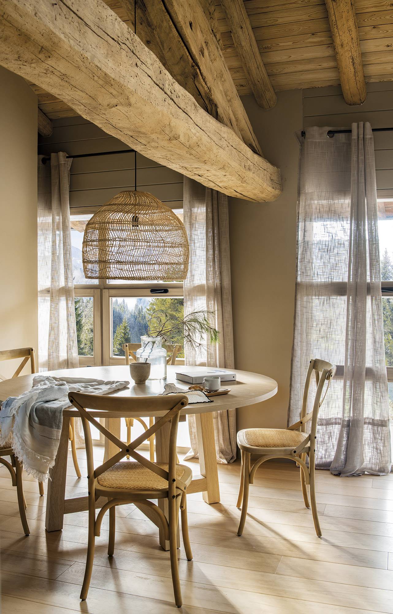 Comedor rústico con mesa redonda con sillas de madera y vigas en el techo.
