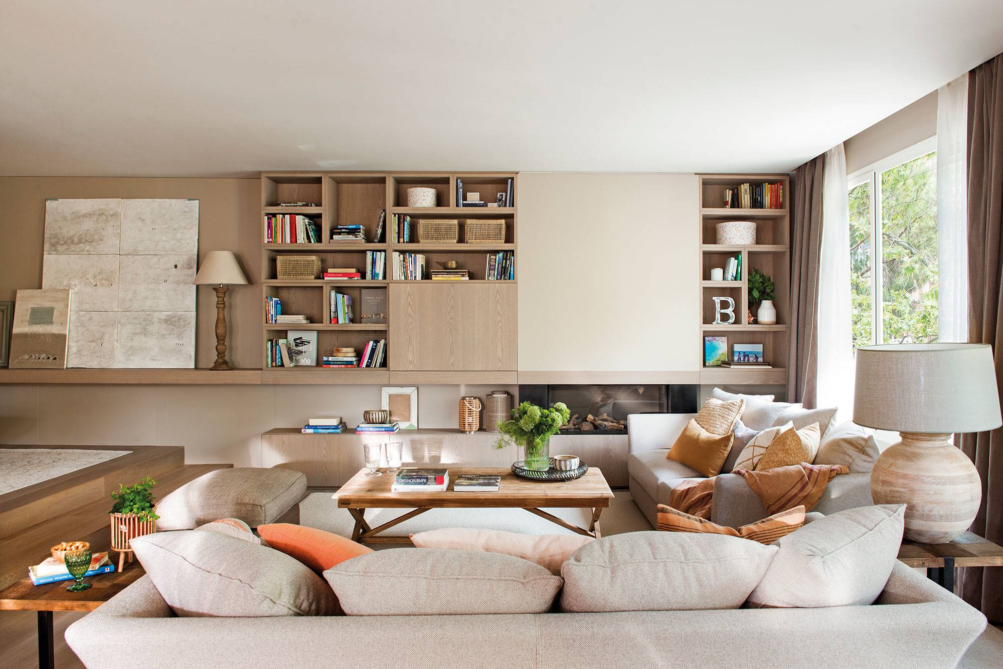 Salón con mueble que integra librería, tele y estantes, y dos sofás en beige. 