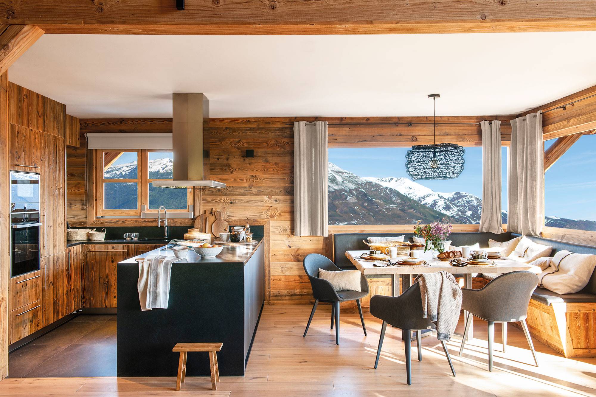 Cocina comedor de cabaña de madera con vistas a las montañas nevadas.