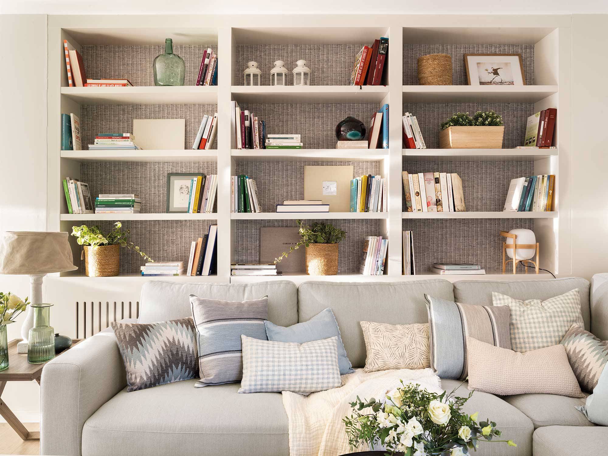 Salón con librería con trasera empapelada y sofá gris. 