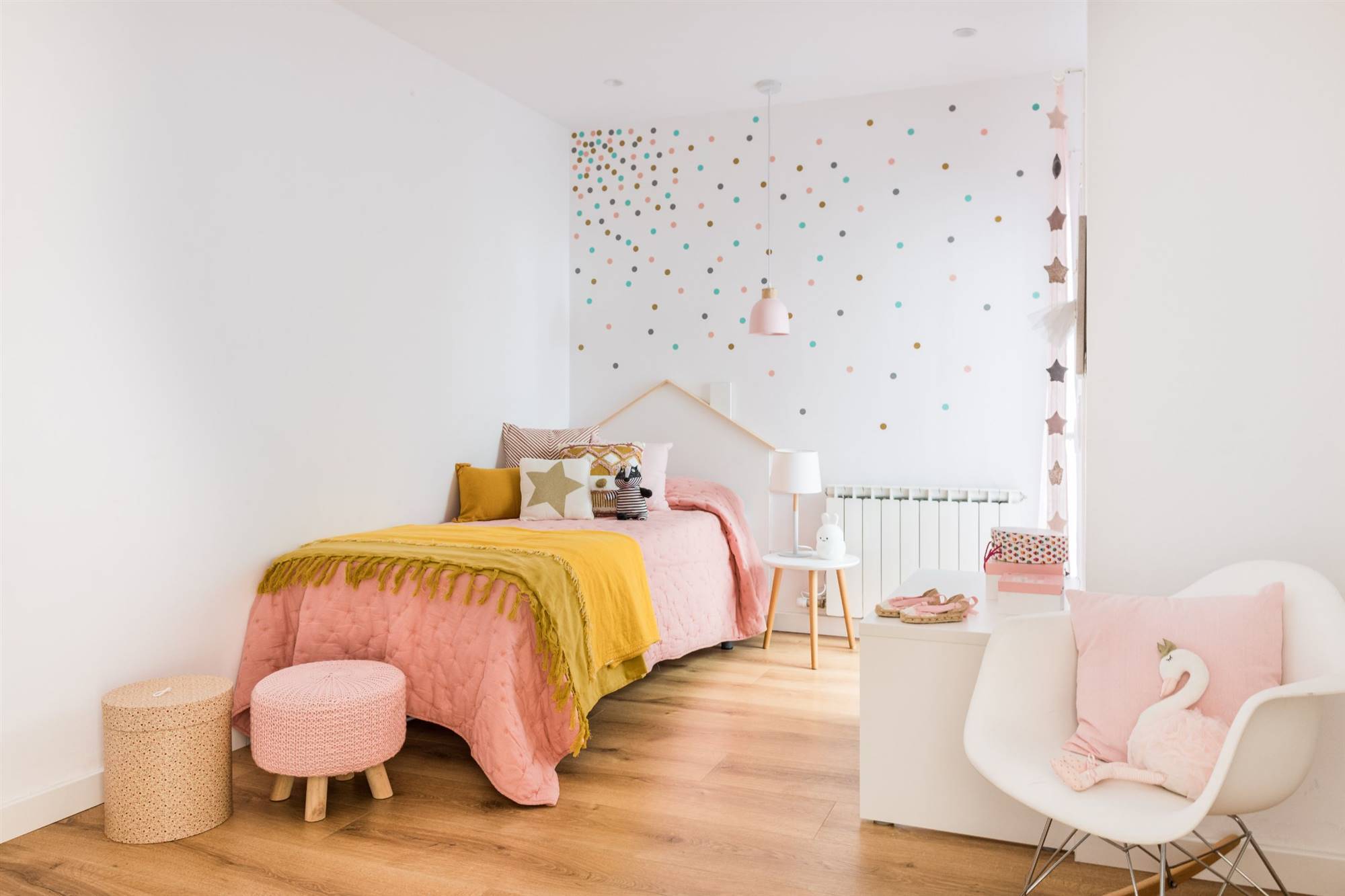 Habitación infantil después de la reforma con cama, decoración en la pared, butaca blanca y taburete rosa. 