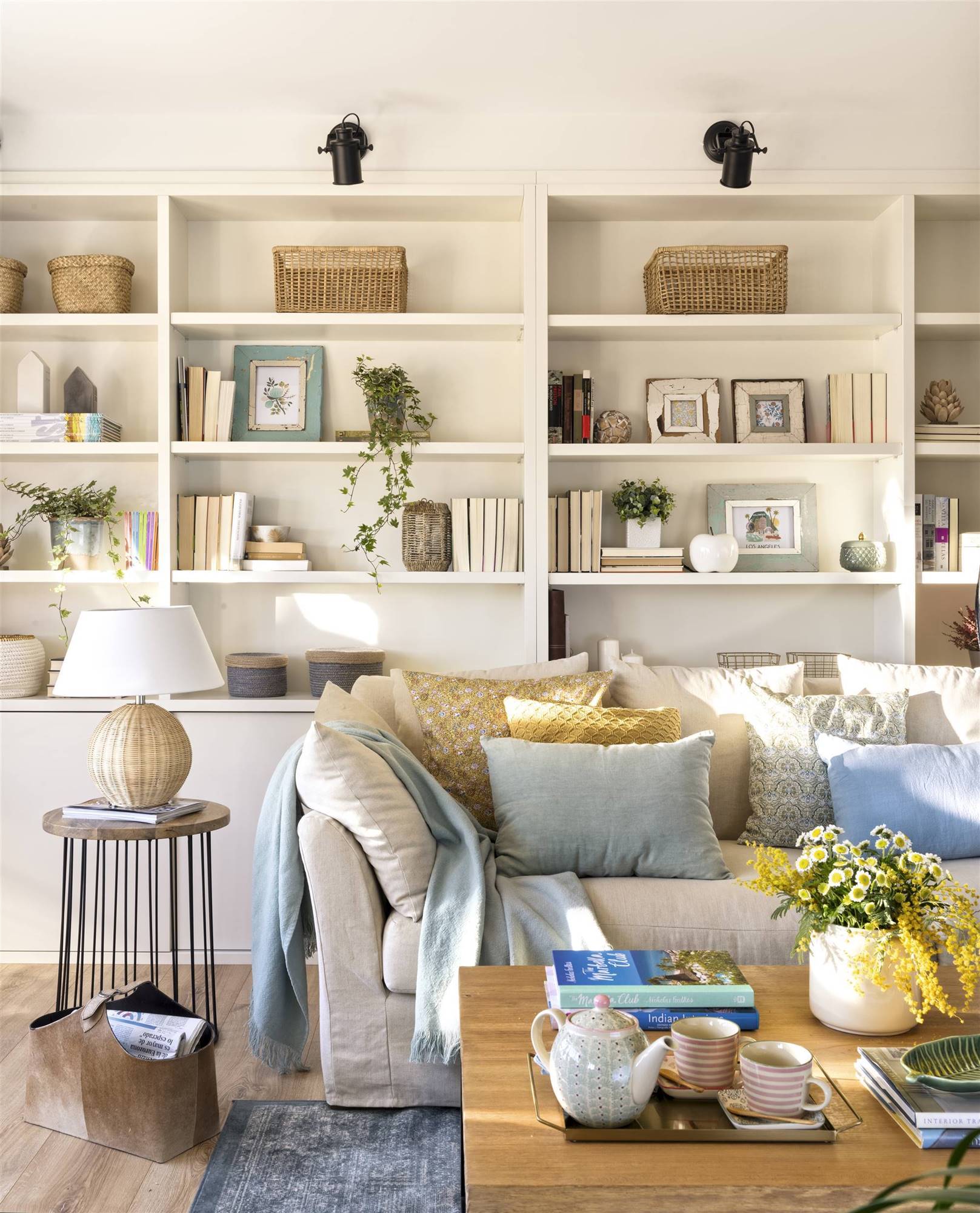 Salón con librería blanca, sofá beige y mesita auxiliar de hierro y madera. 