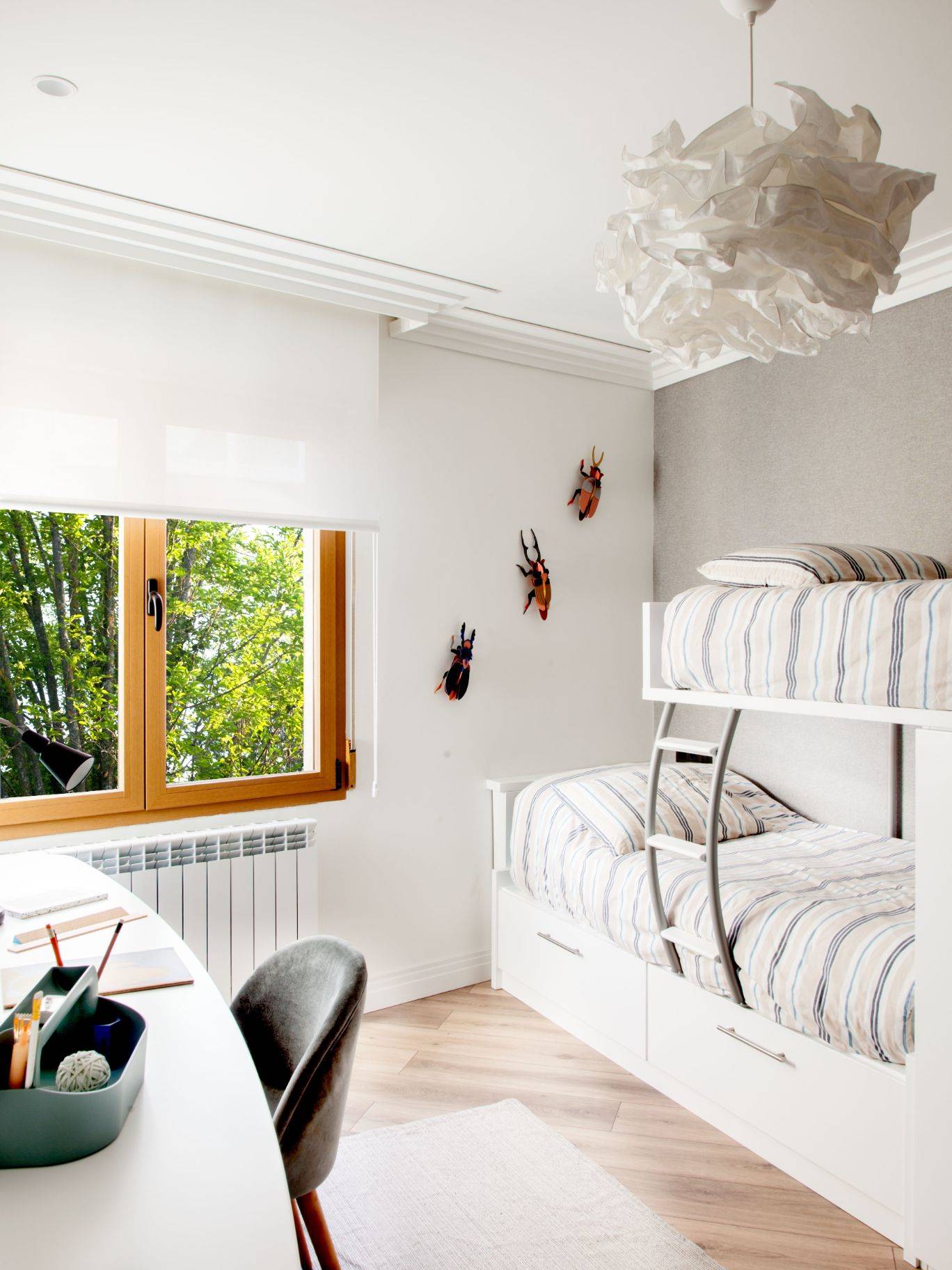 Dormitorio infantil con litera, escritorio curvo, suelo de madera y decoración de pared de insectos. 
