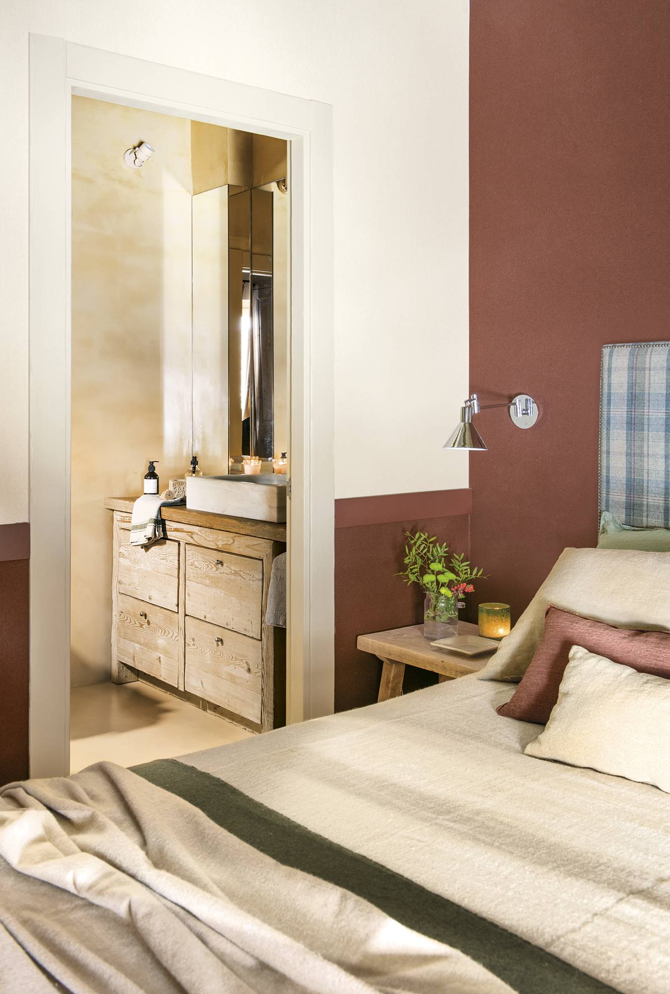 Dormitorio principal con mesita de noche de madera, cabecero tapizado, pared granate y acceso al baño 