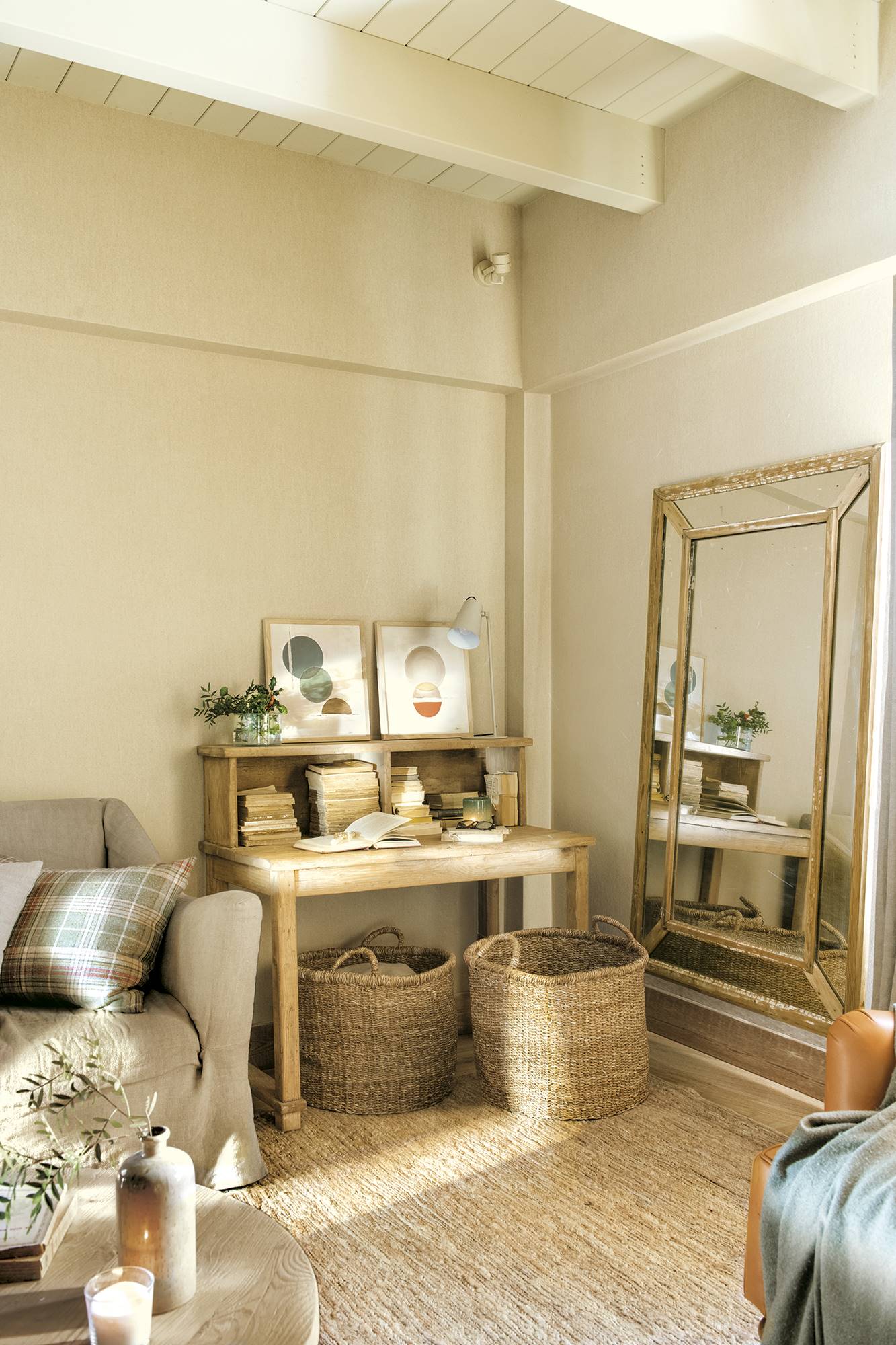 Rincón en el salón con espejo en el suelo grande, cestas de fibras naturales, alfombra de fibras y escritorio de madera.