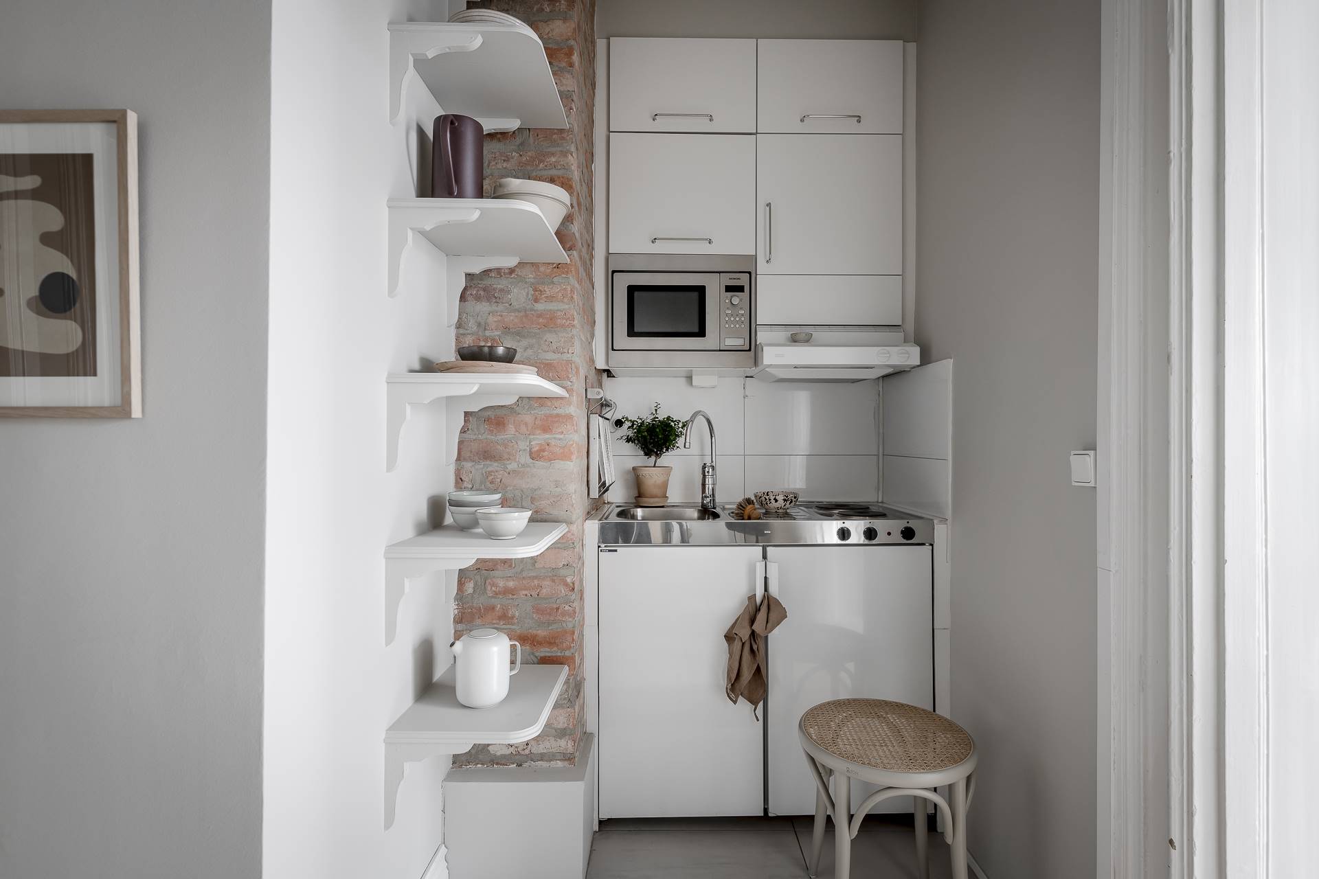Cocina blanca pequeña con pared de ladrillo visto y baldas flotantes